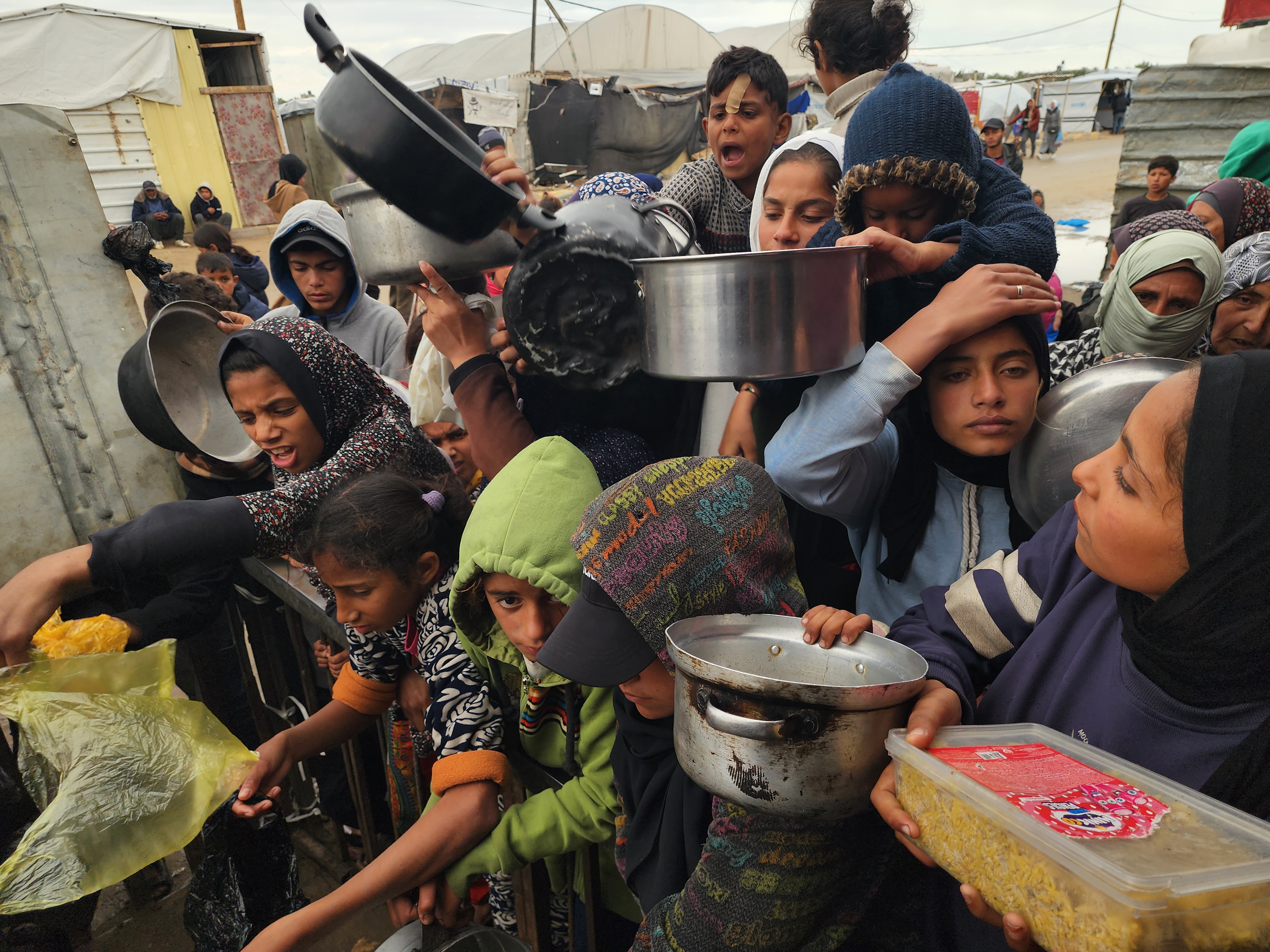 Palestinians wait with empty containers in their hands to receive food distributed by charitable organisations.