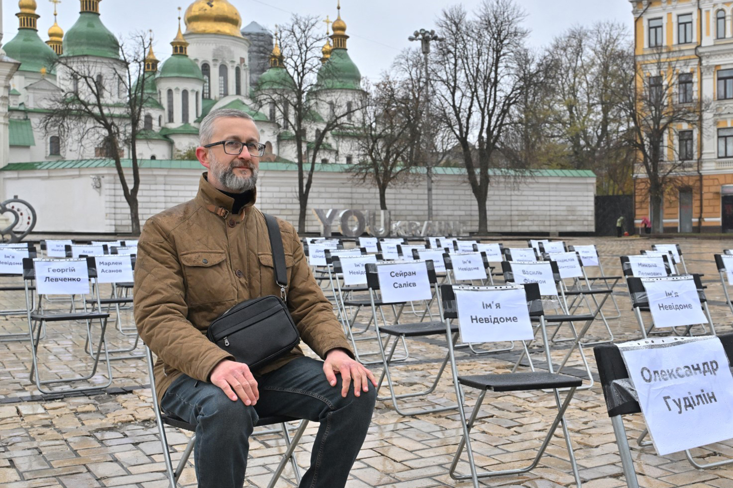 Nariman Dzhelyal sits on a chair before rows of chairs displaying the names of journalists, writers, cultural figures and human rights activists.