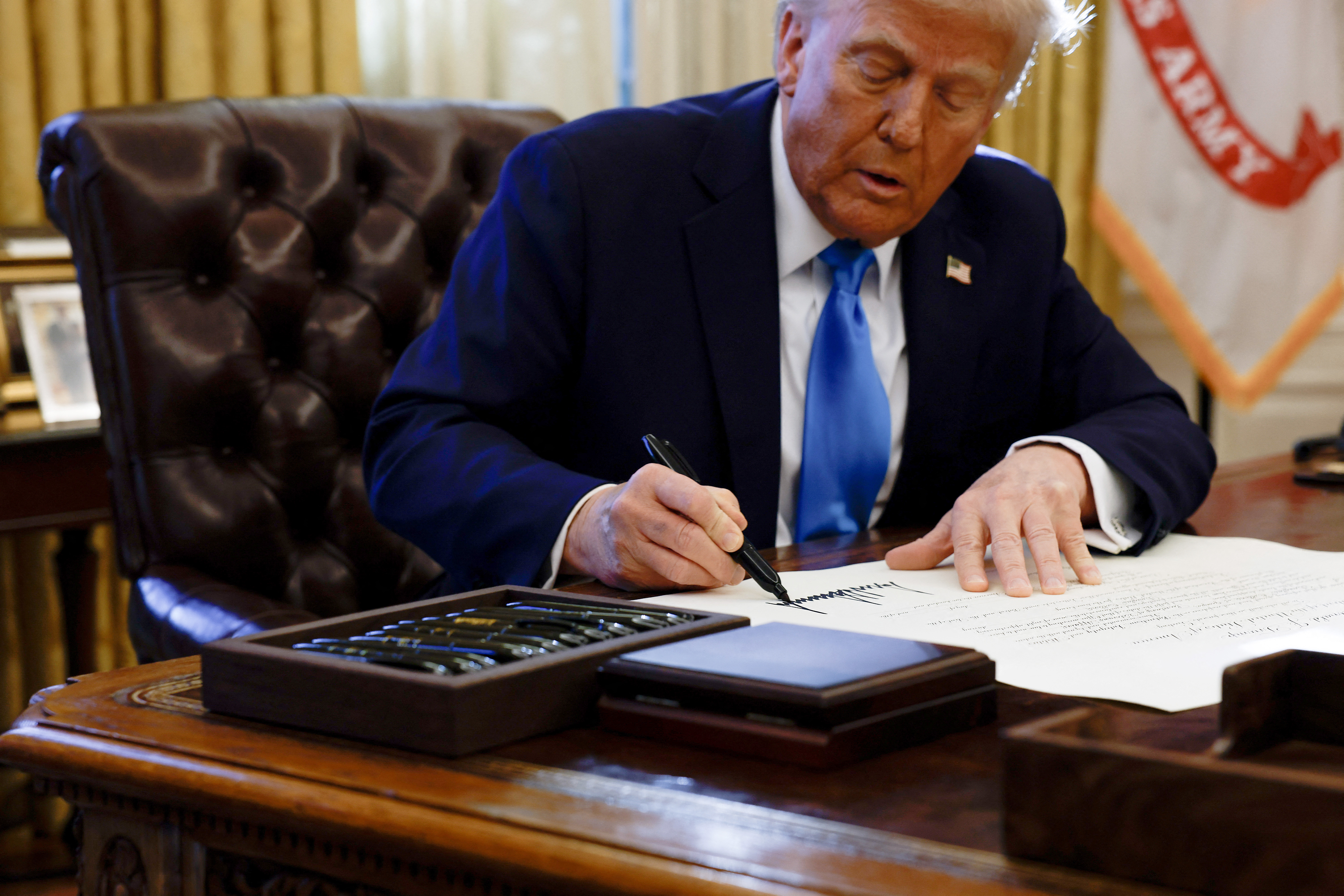 Trump signs an executive order at the Oval Office desk.