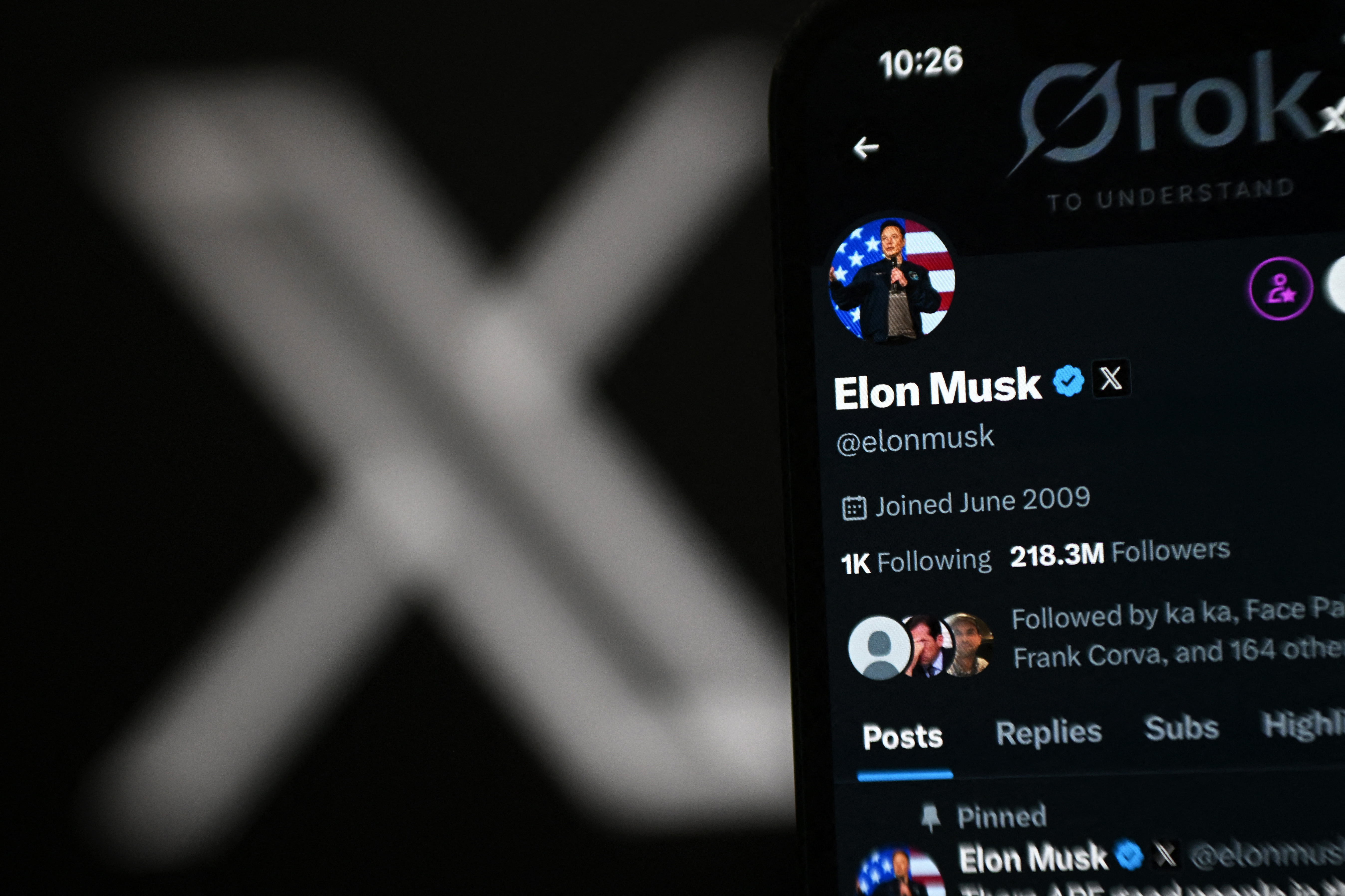 X account of Elon Musk displayed on a phone screen next to the X logo displayed on a laptop screen