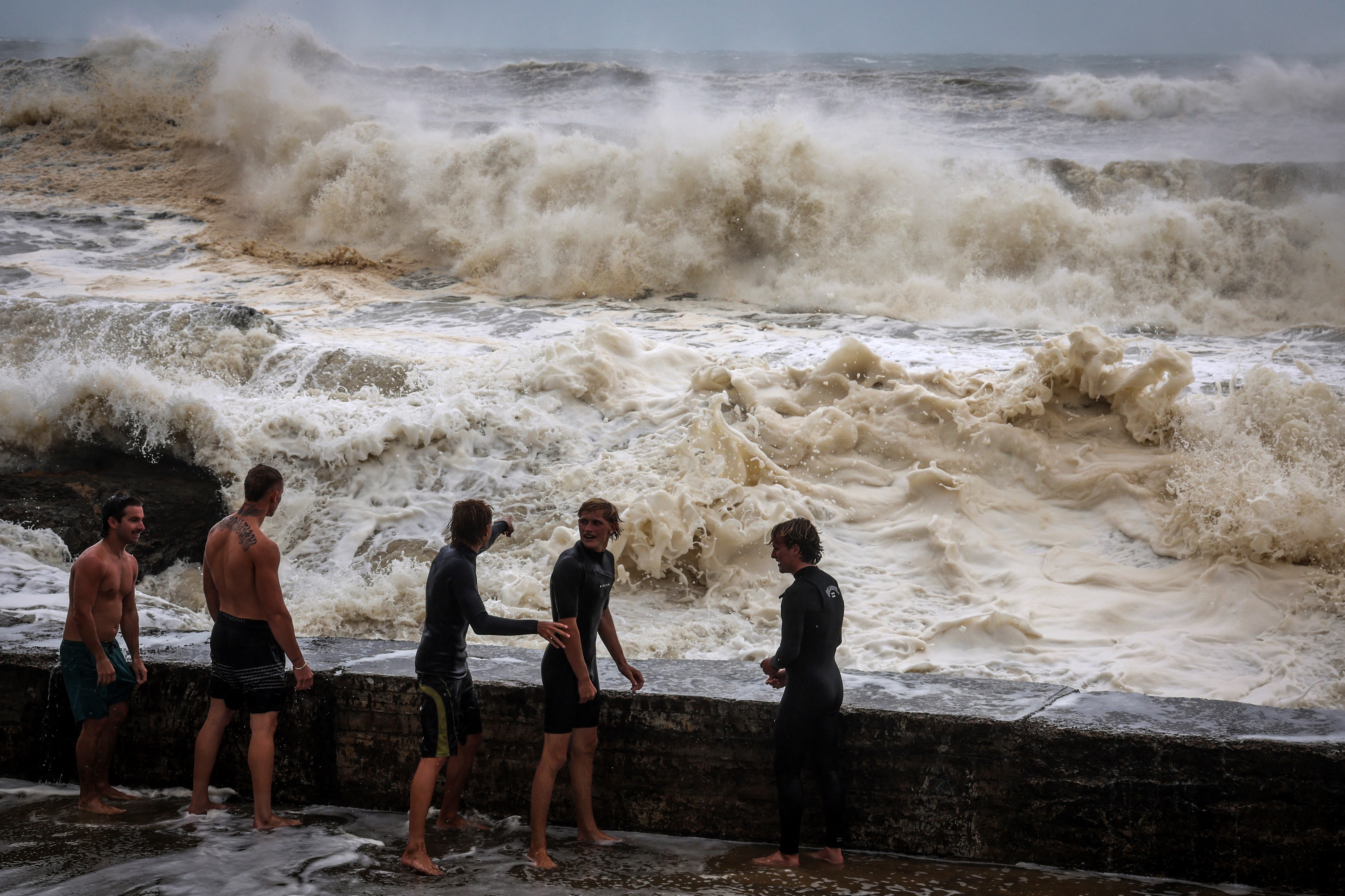 Young men stand behind a wall as they play in record-breaking waves caused by the outer fringe of Tropical Cyclone Alfred at Point Danger in Coolangatta on March 7, 2025
