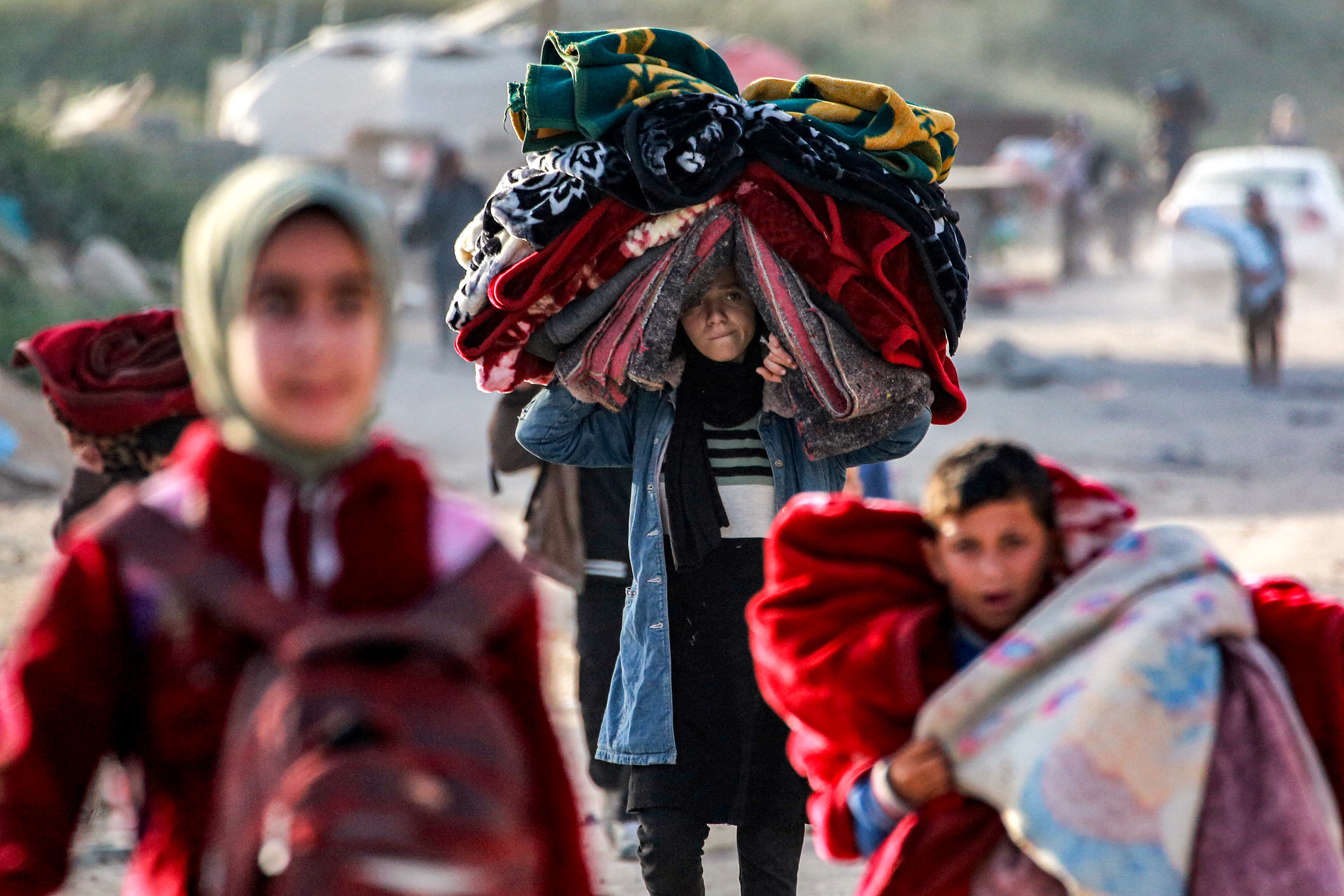 A girl carrying a pile of blankets on her head walks with others displaced by conflict and fleeing from Beit Hanun in the northern Gaza Strip as they arrive with their belongings in Gaza City on March 18, 2025. Israel on March 18 unleashed its most intense strikes on the Gaza Strip since a January ceasefire, with rescuers reporting 220 people killed, and Hamas accusing Benjamin Netanyahu of deciding to "resume war" after a deadlock on extending the truce. (Photo by Bashar TALEB / AFP)