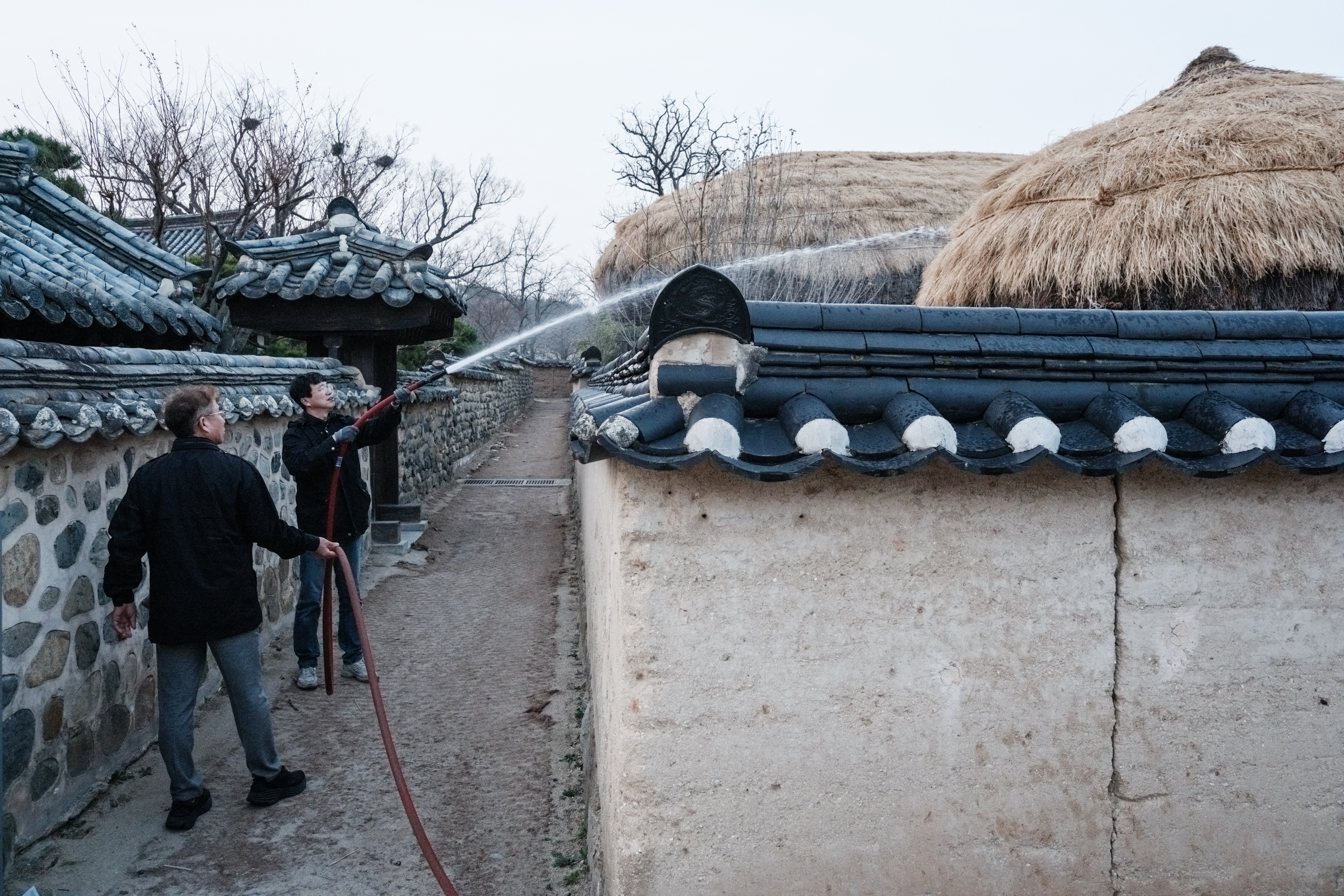 A man sprays water onto a thatched roof for the approaching wildfire in Andong Hahoe Folk Village, in Andong, South Korea, on March 25, 2025. Inhabitants of a UNESCO-listed village were ordered to evacuate while a historic Buddhist temple was burned to the ground as South Korea scrambled to contain worsening wildfires, which are tearing across the country's southeast. (Photo by Yasuyoshi CHIBA / AFP)