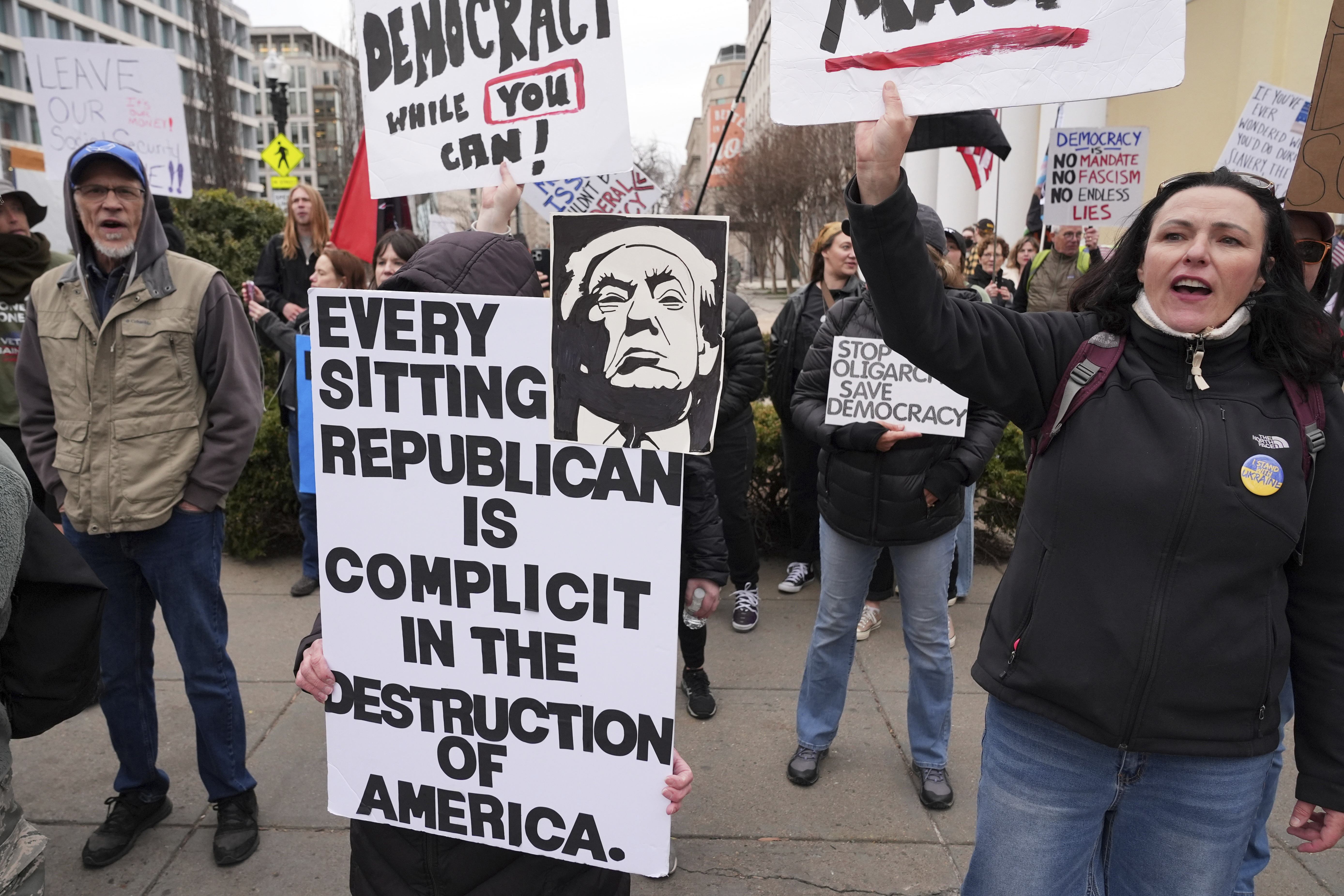 Protesters demonstrate outside the White House. One holds a sign that reads, "Every sitting Republican is complicit in the destruction of America."