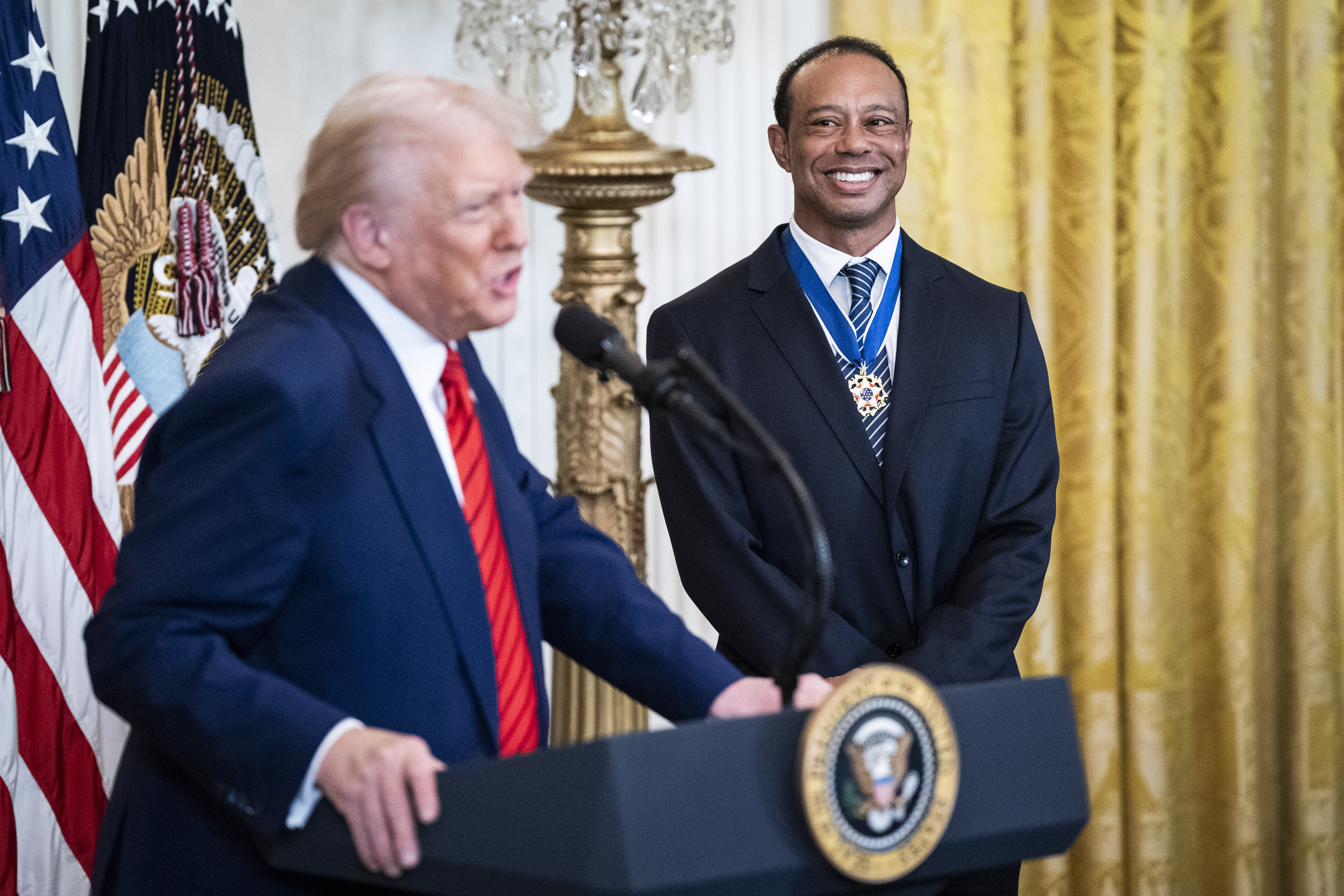 Donald Trump and Tiger Woods speaking at a ceremony.