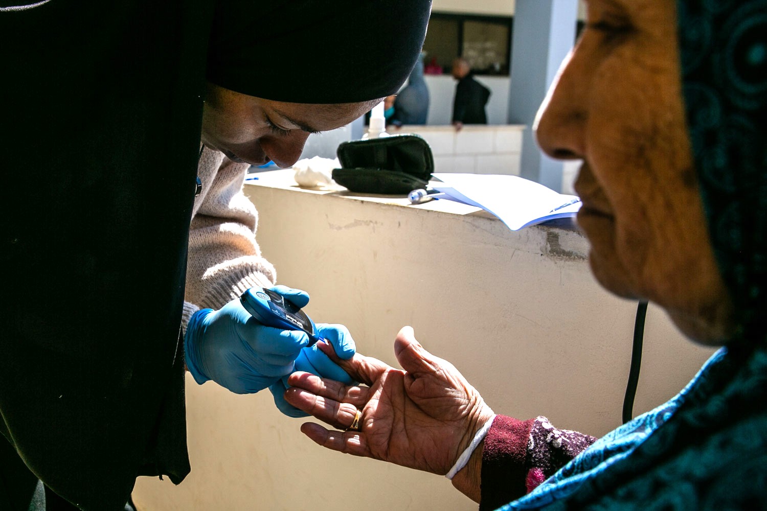 Omaima bends to take a blood sugar reading for an elderly displaced woman.