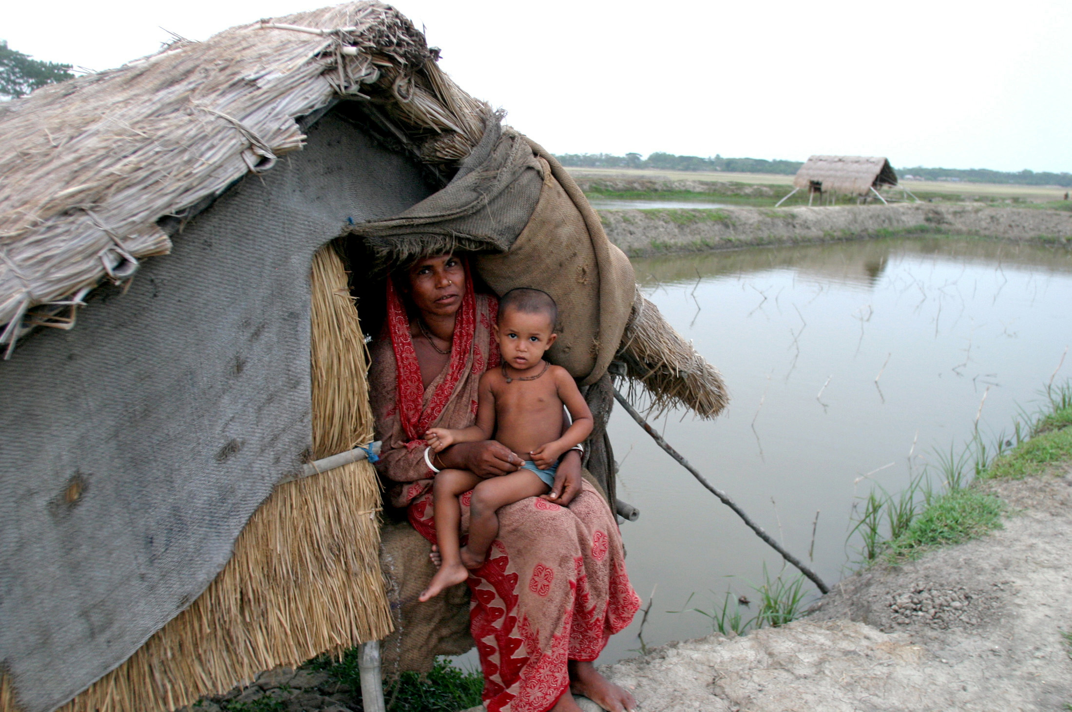 A Bangladeshi woman sits in a makeshift hut with her son near a shrimp farm in Munshiganj