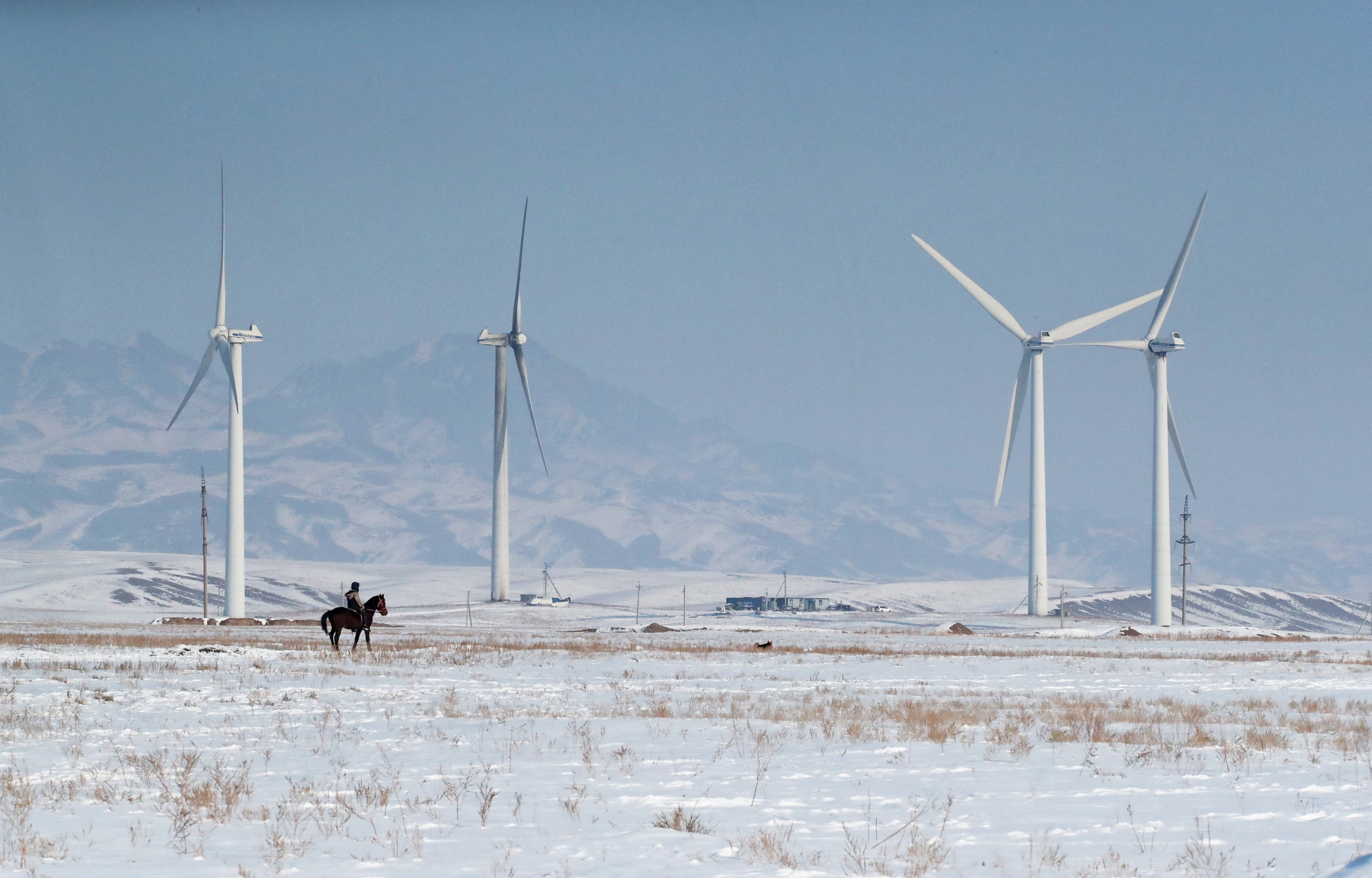 A man rides a horse near a wind power plant in the Almaty region, Kazakhstan