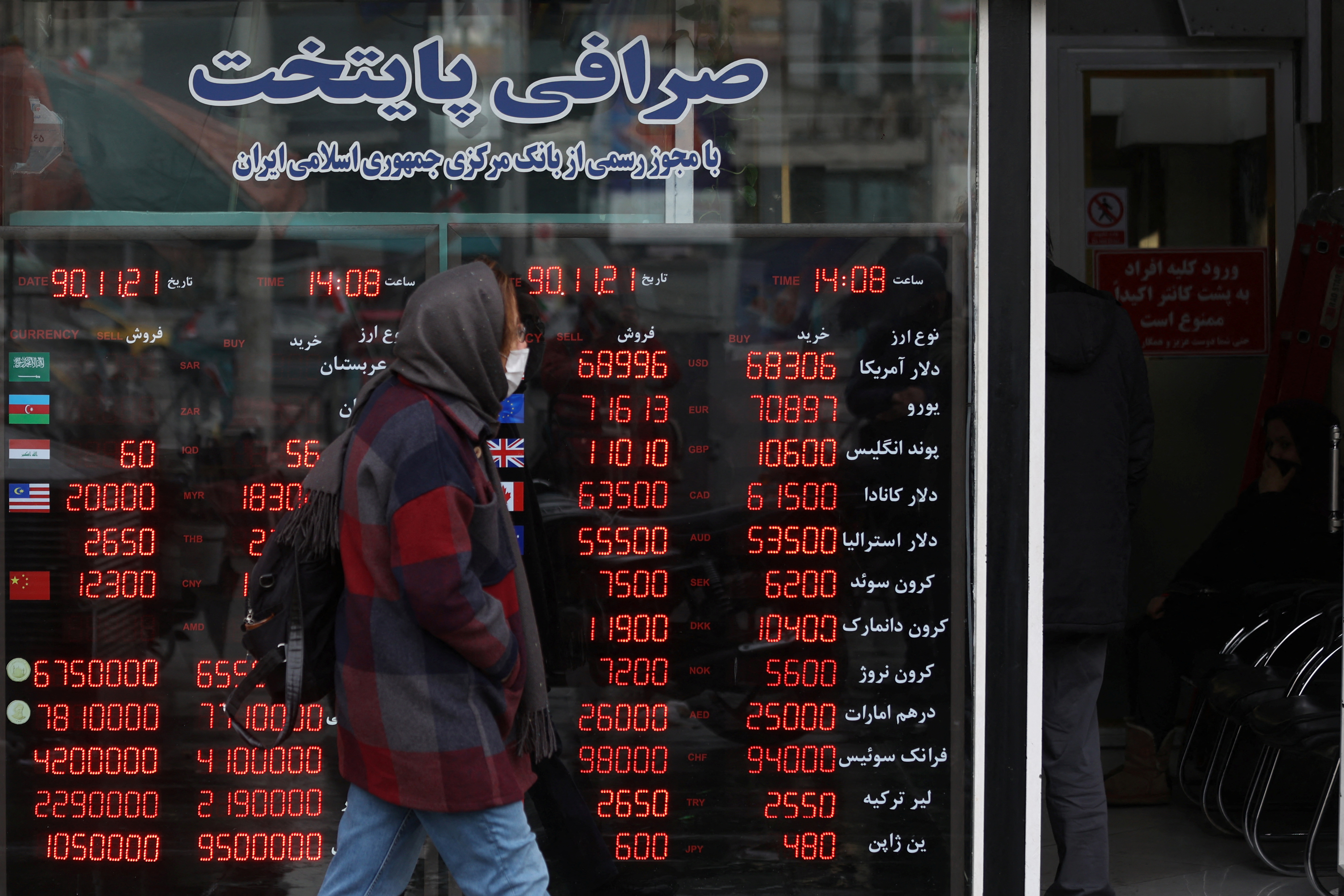 People walk past a sign at a currency exchange as the value of the Iranian Rial drops, in Tehran