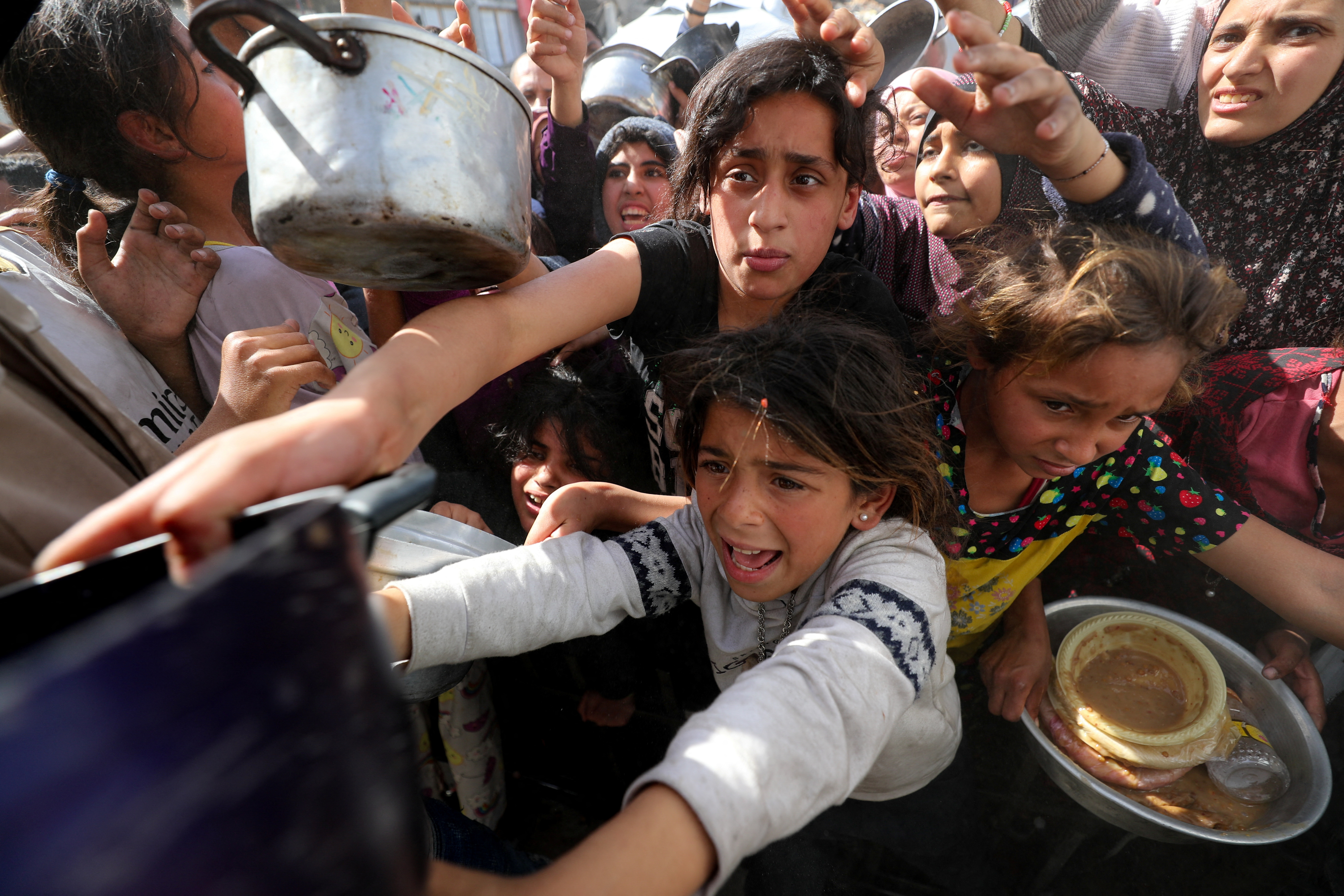 Palestinian children wait to receive food cooked by a charity kitchen.