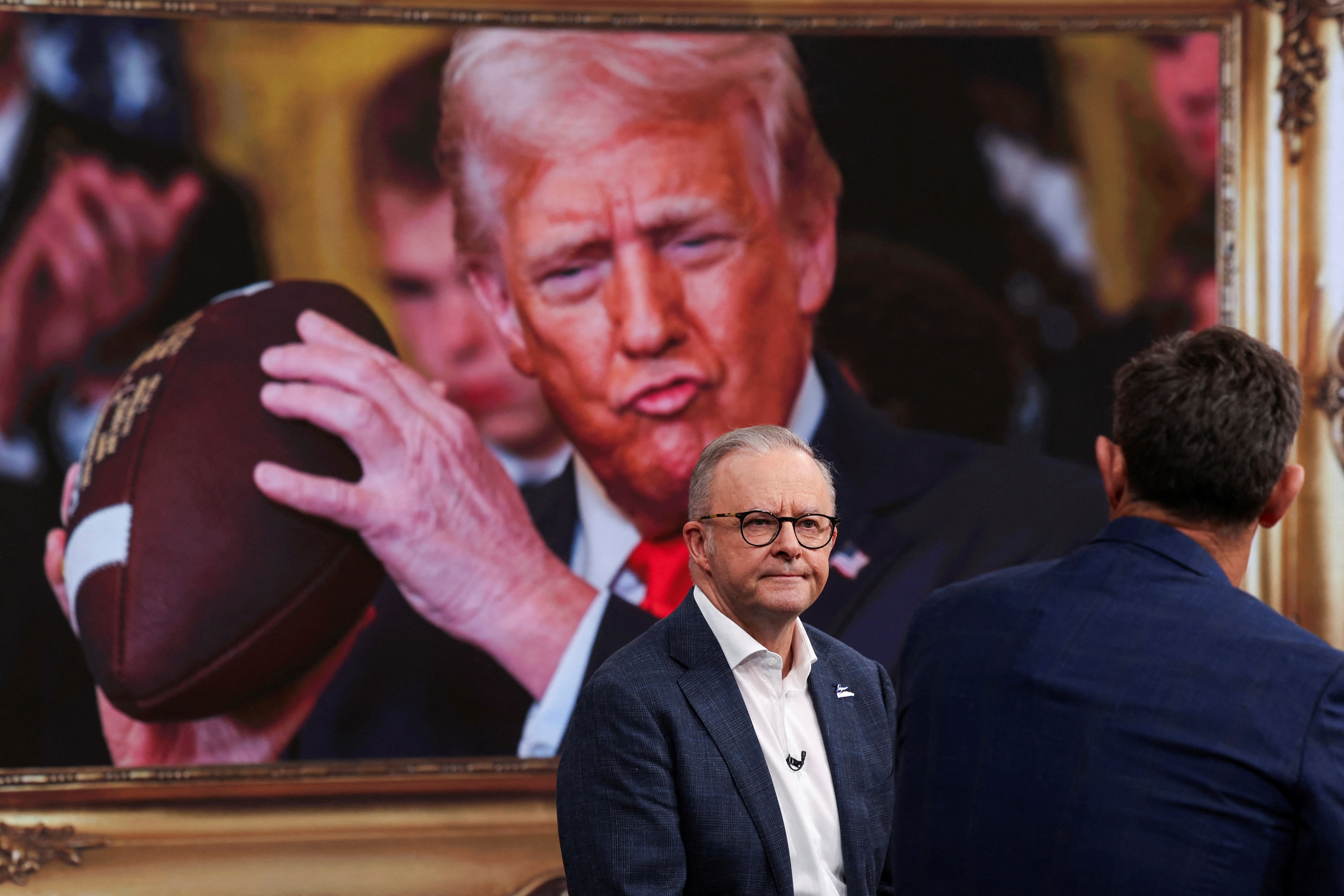 Prime Minister Anthony Albanese looks on in front of an image of US President Donald Trump.