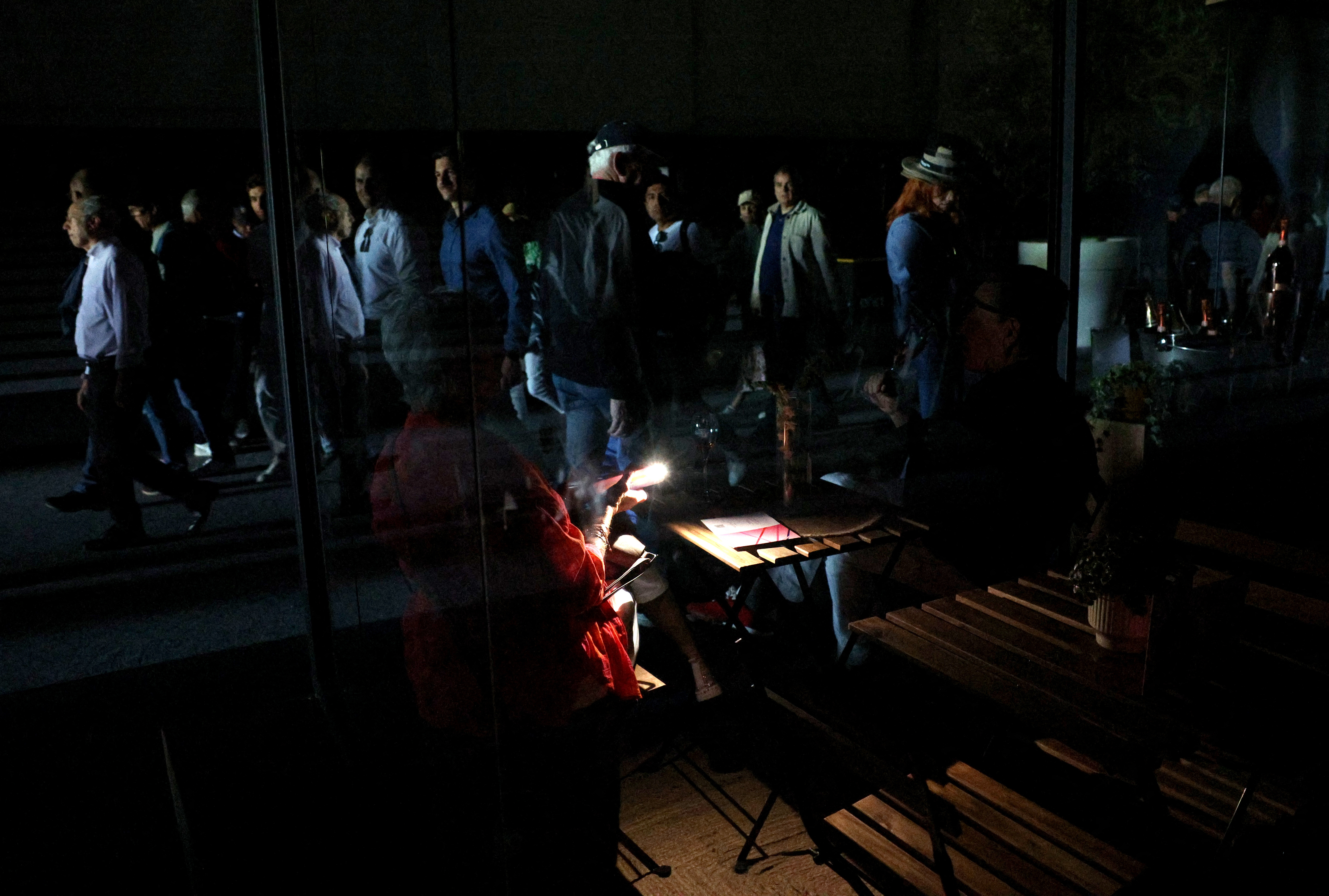Madrid Open - Park Manzanares, Madrid, Spain - April 28, 2025 A woman uses her cell phone's flashlight in the dark after the matches get suspended due to a power outage. [Violeta Santos Moura/Reuters]