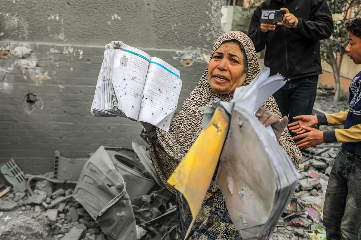 a woman holds damaged books as she stands in rubble