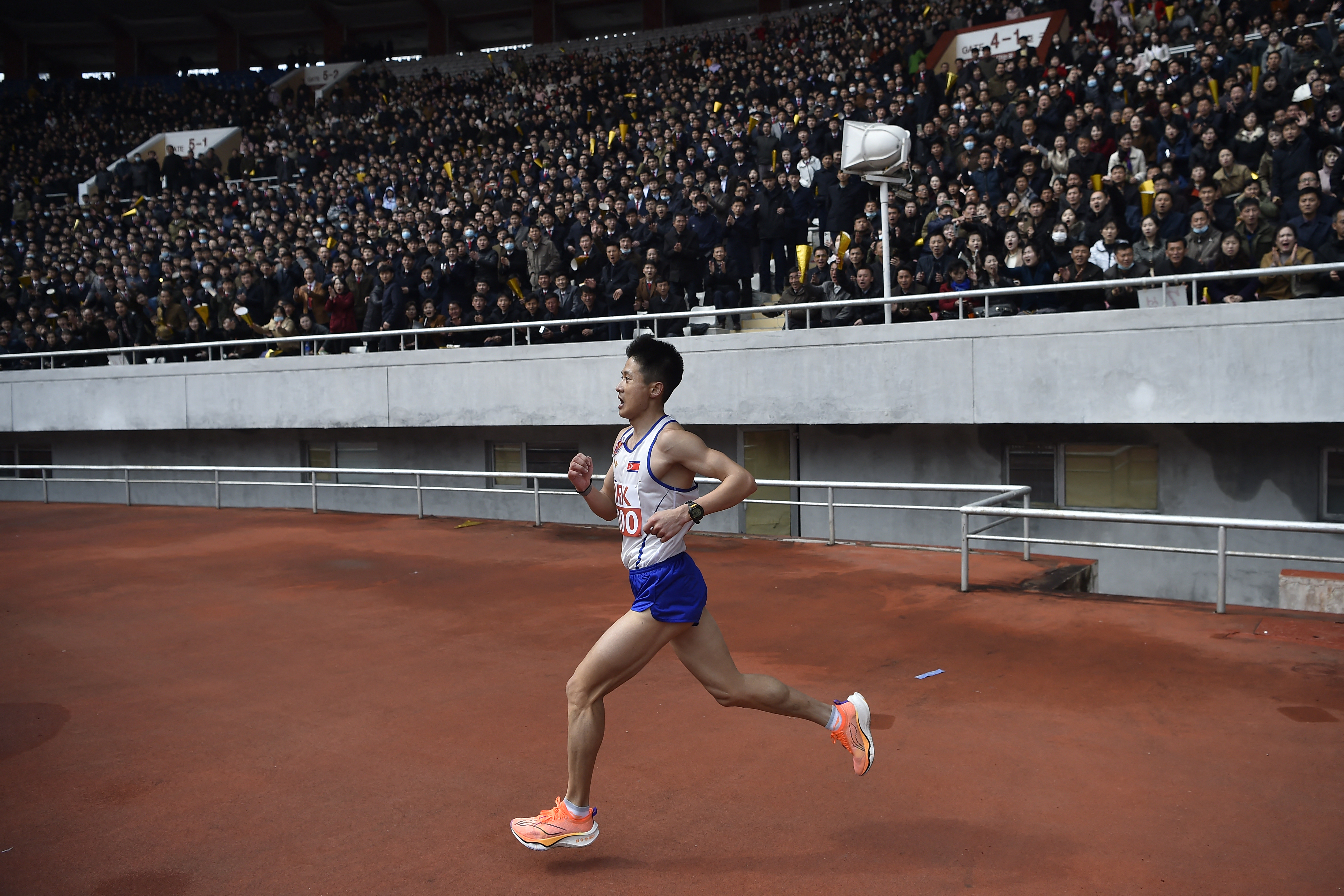 An athlete runs onto the track with the crowd in the background in the stands.