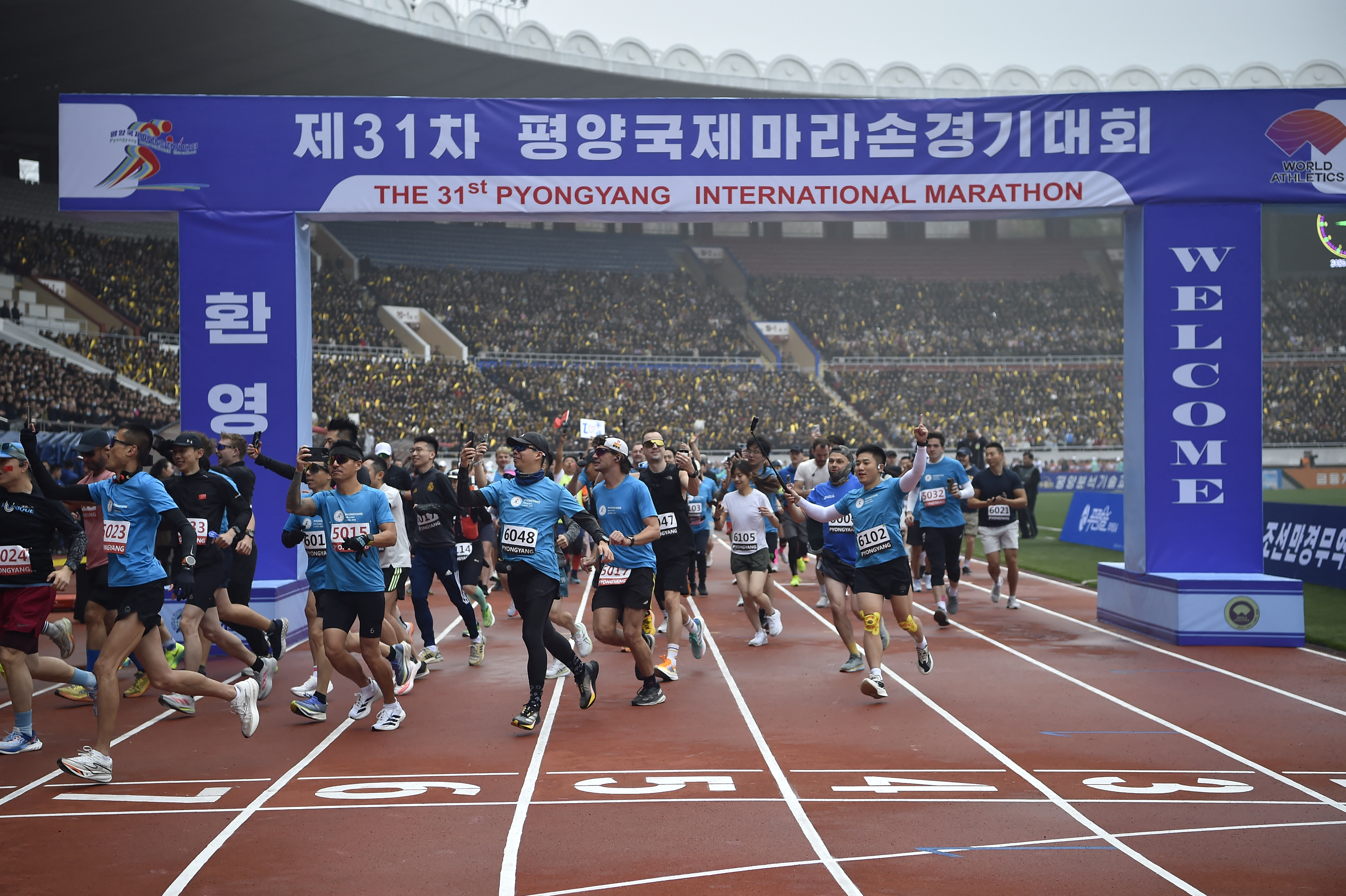 Runners holding mobile phones, dressed in blue, run through the track.