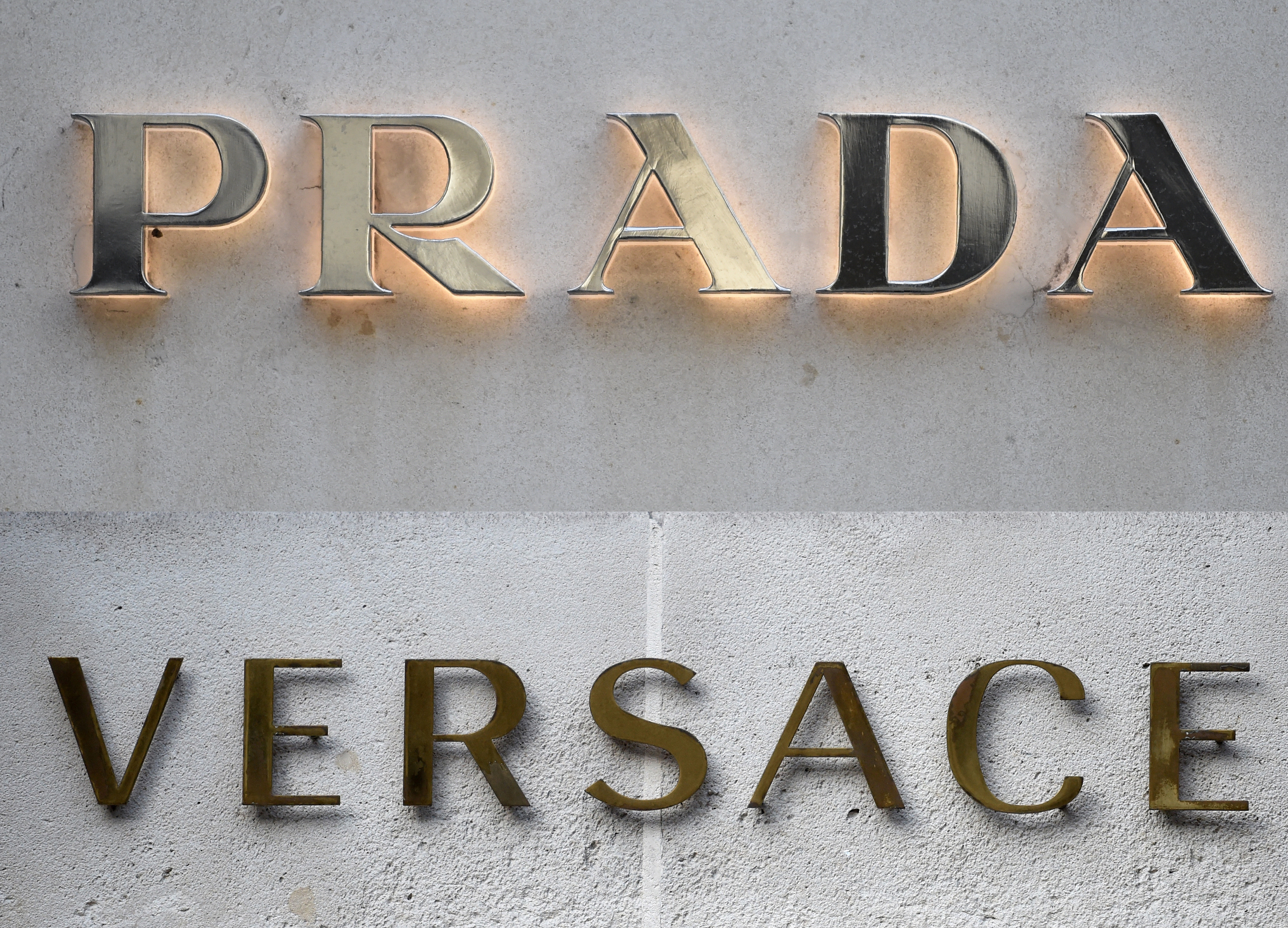 Logos of Versace and Prada in front of two stores in Paris. [File Stephane De Sakutin/AFP] (Photo by STEPHANE DE SAKUTIN / AFP)