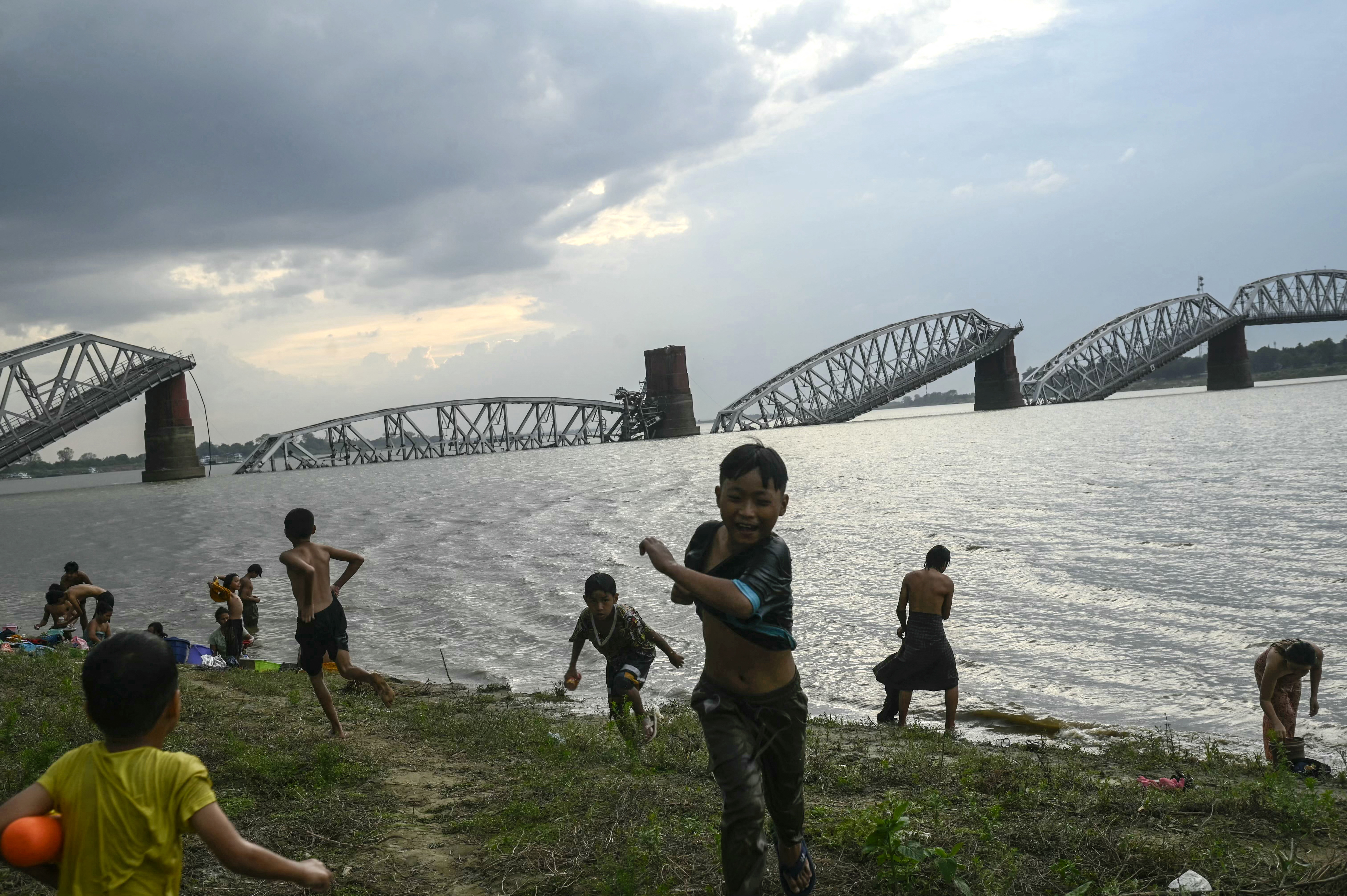People gathered on the banks of the Irrawaddy River in front of the collapsed Ava Bridge, also known as the Inwa Bridge, in Mandalay on April 13, 2025, days after an earthquake struck central Myanmar. (Photo by Sai Aung MAIN / AFP)