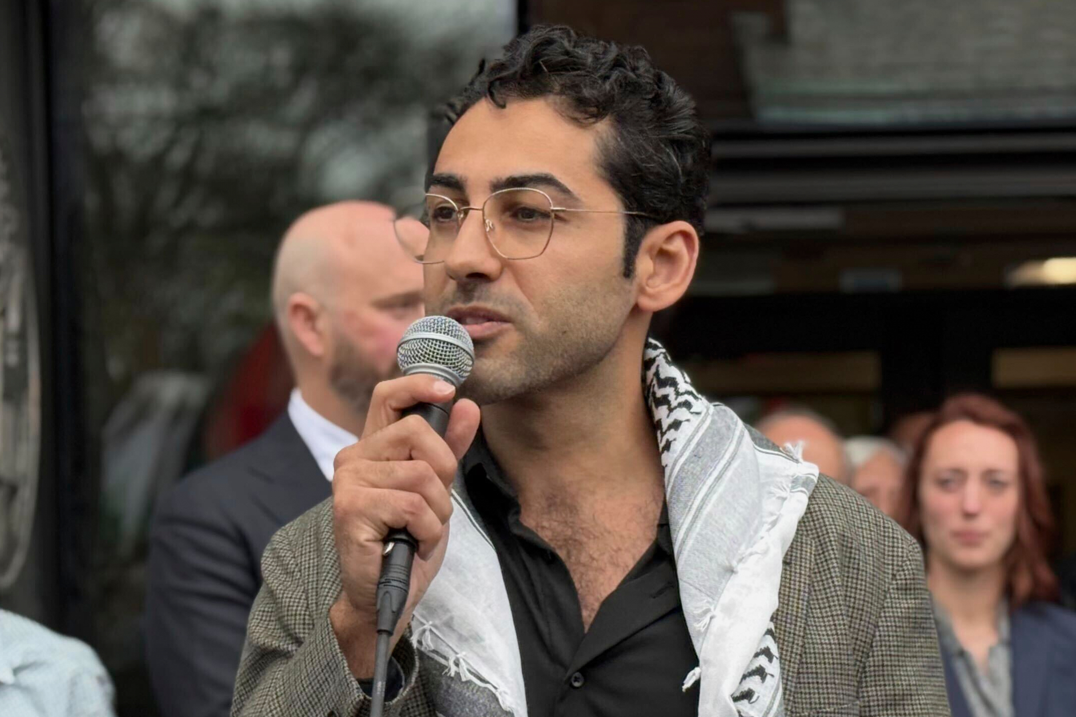 Mohsen Mahdawi speaks into a microphone outside a Vermont courthouse, a keffiyeh draped on his shoulders.
