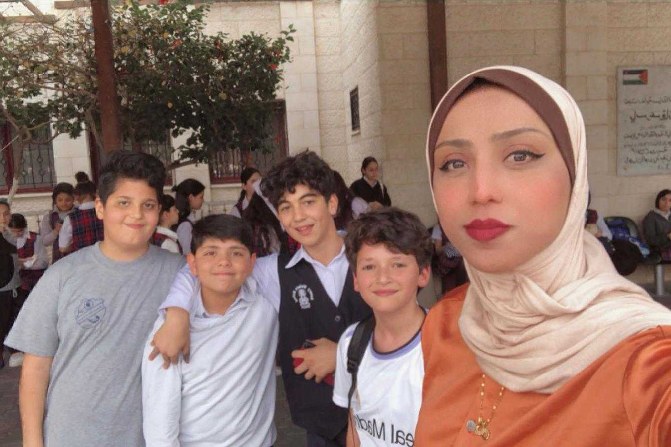 A hijabi woman appearing in the right side of the photo takes a selfie with four little boys