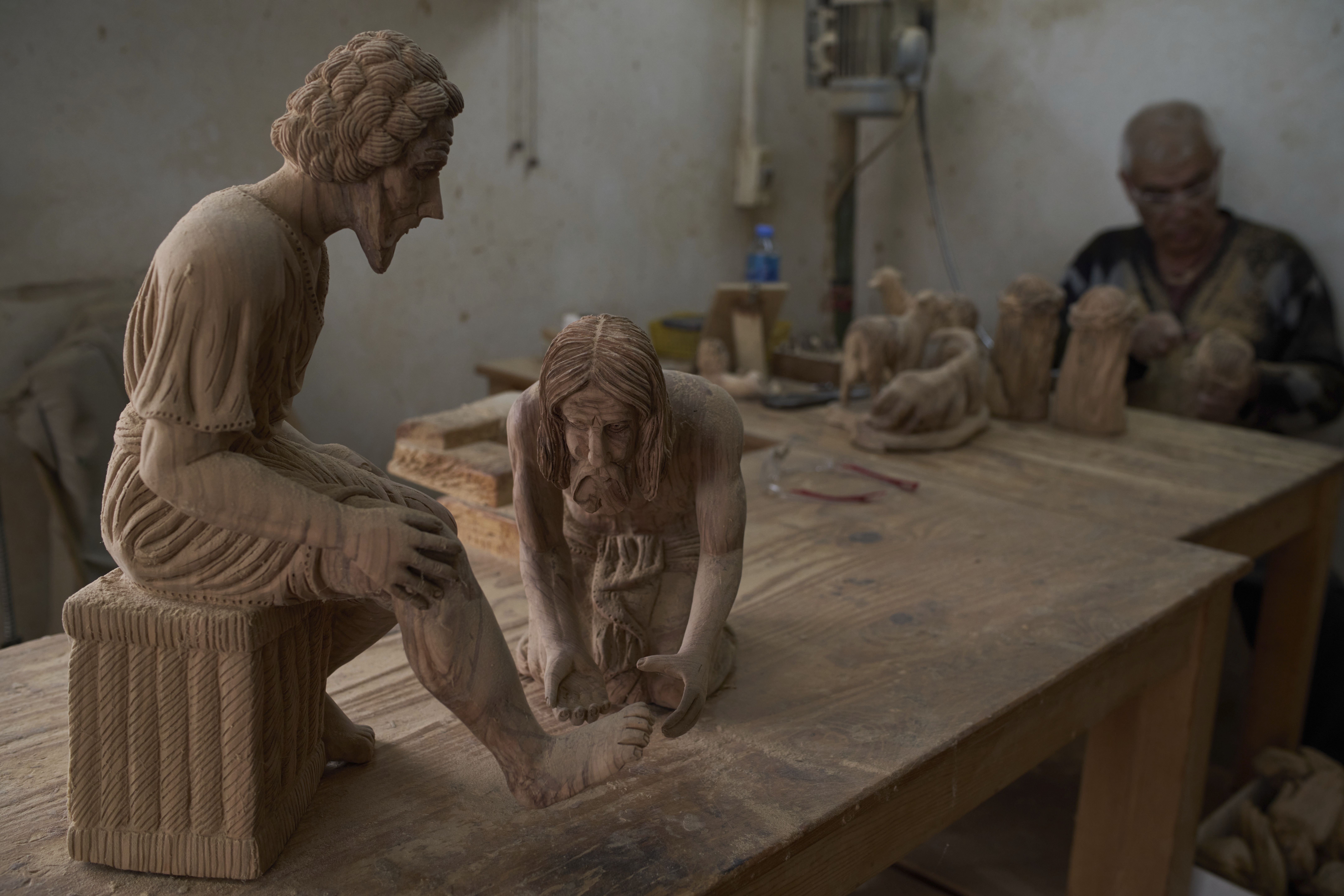 A Palestinian carver works on a biblical figurine made from olive wood as he sits next to sculptures depicting the Washing of the Feet scene at the Zacharia family workshop prior to Holy Week celebrations in the West Bank city of Bethlehem on Tuesday, April 8, 2025. (AP Photo/Leo Correa)