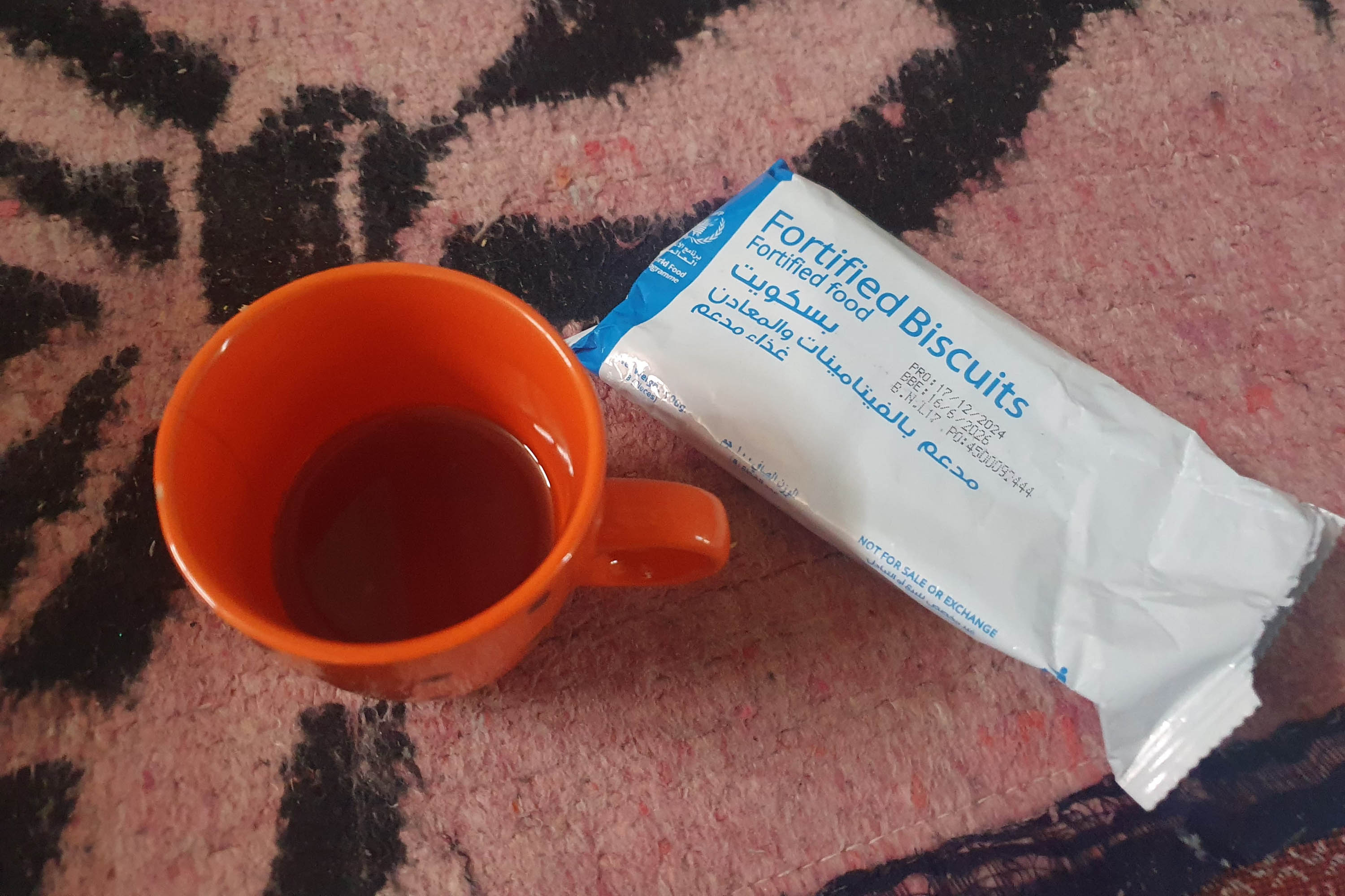 A photo of a red cup of tea and a packaged biscuit from WFP on a table