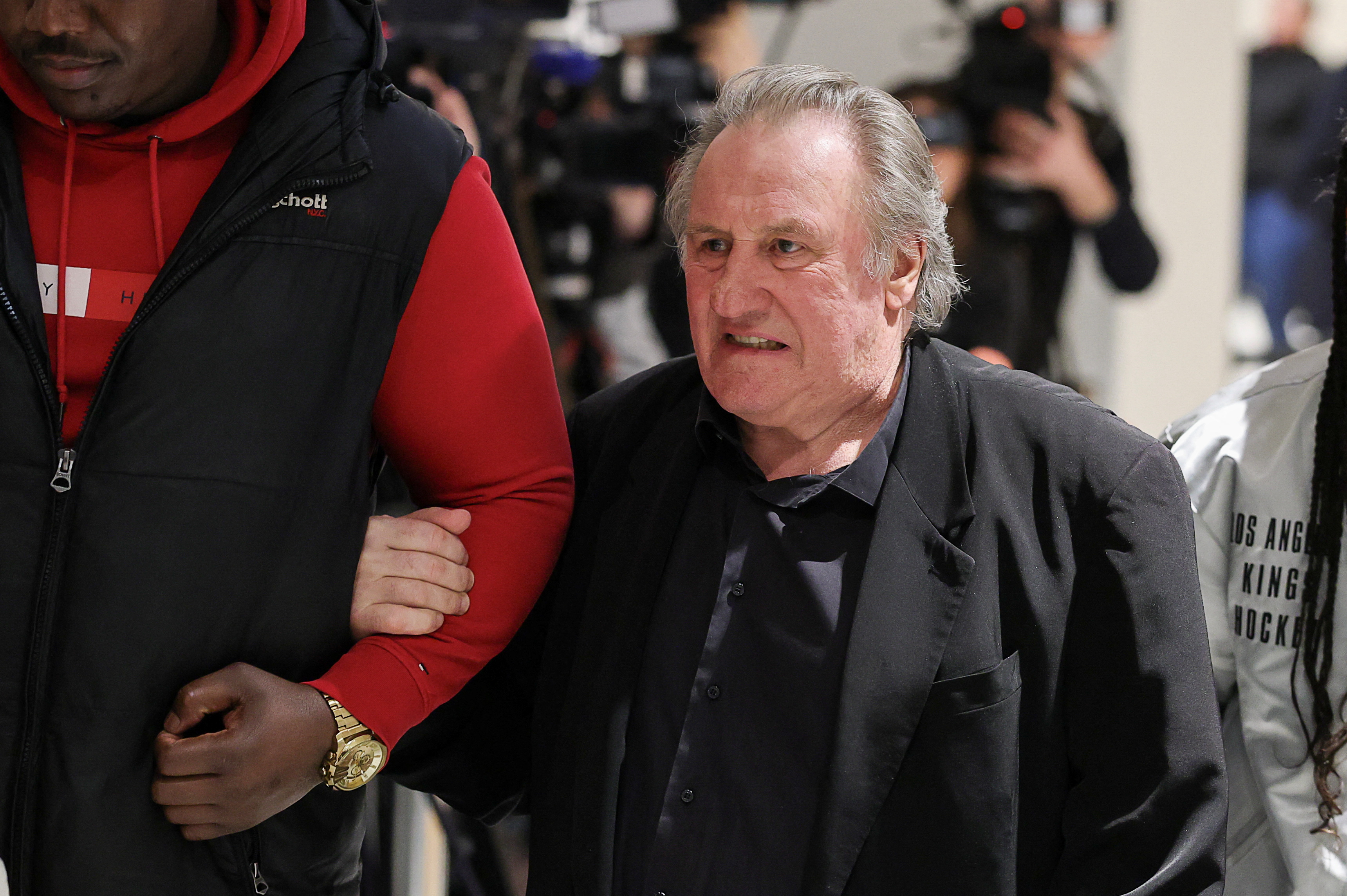 French actor Gerard Depardieu leaning on someone's arm and walking.
