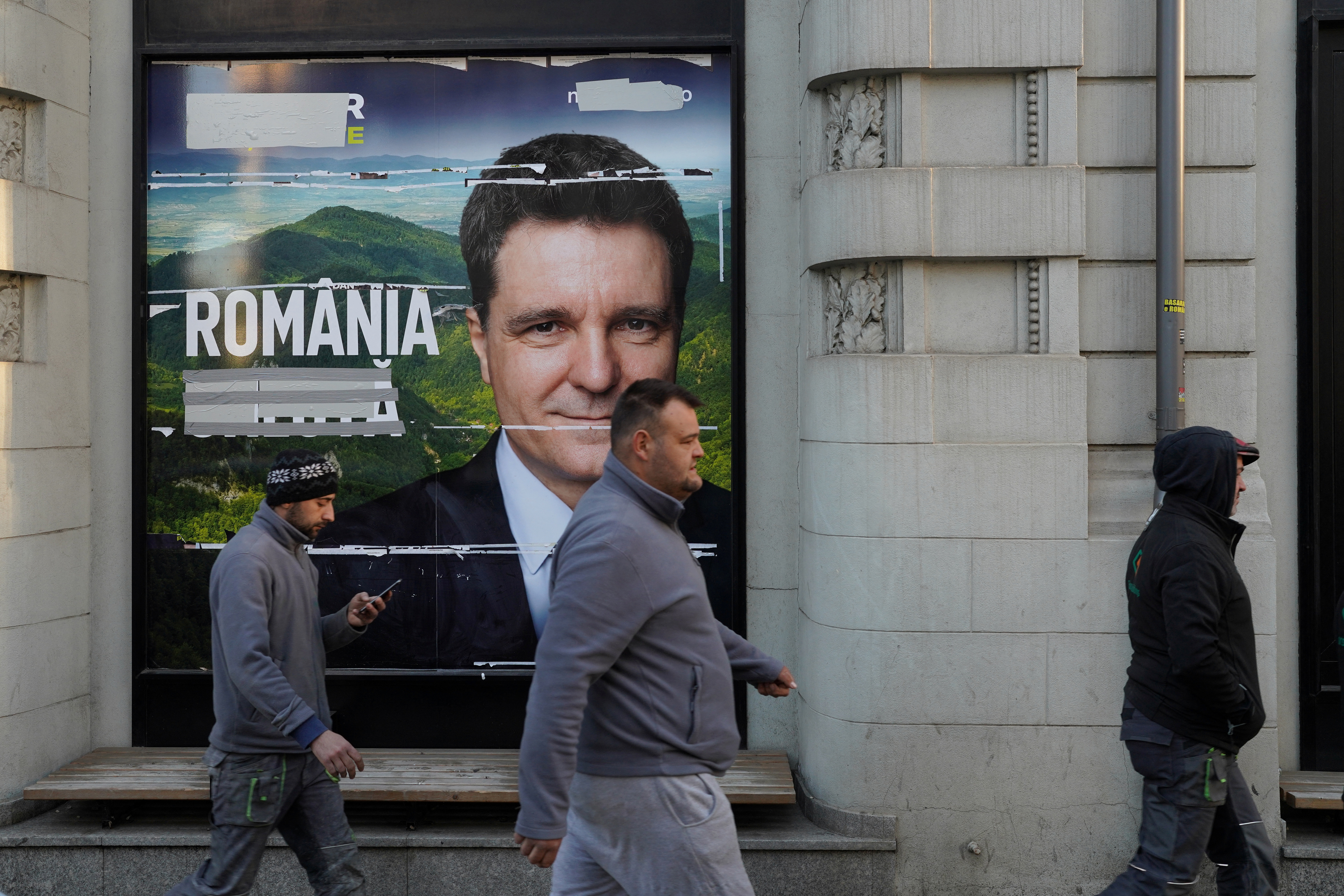 Three men pass by a poster of Nicusor Dan.