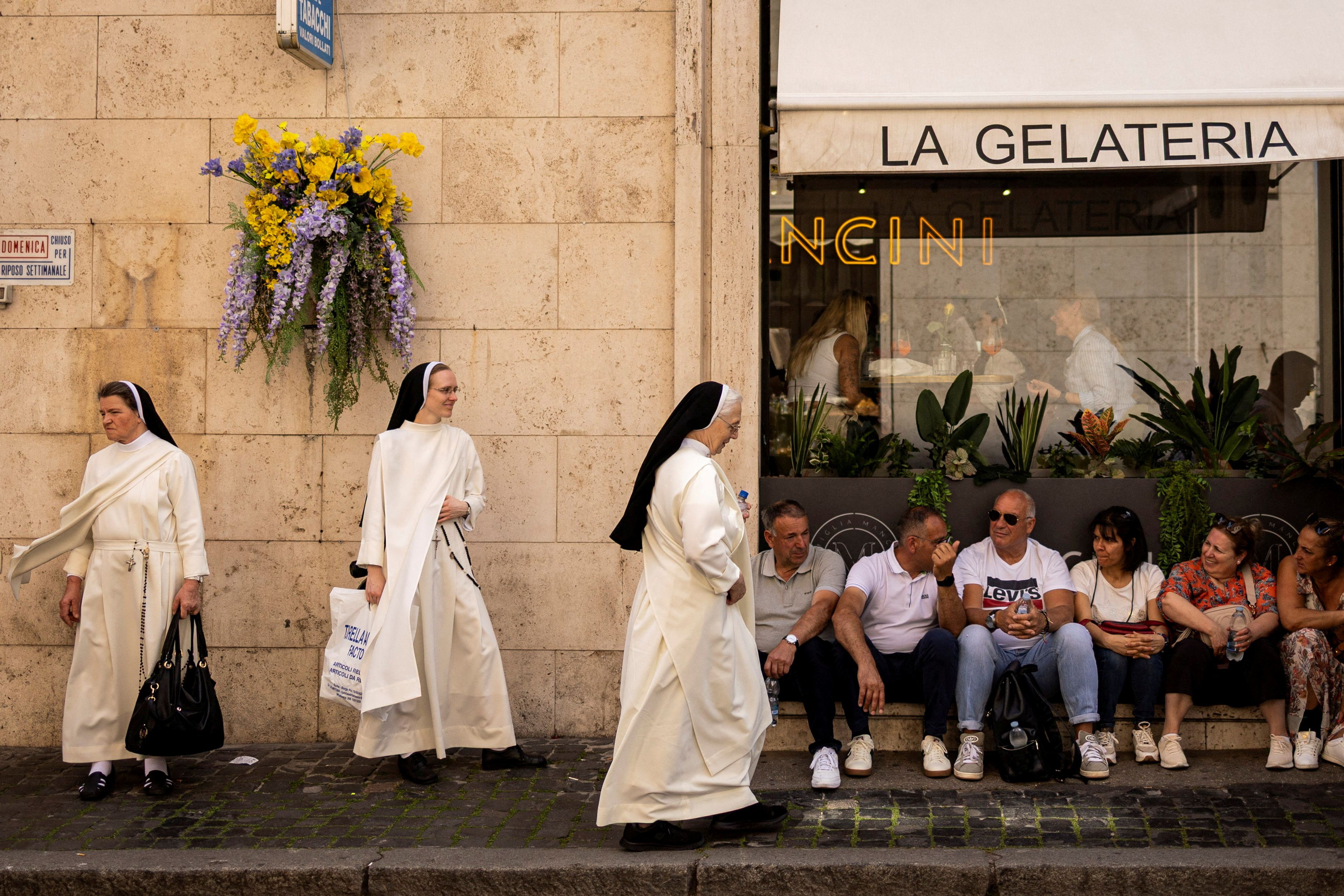 Nuns walk while tourists rest outside a restaurant near the Vatican, ahead of the conclave to elect the next pope, in Rome