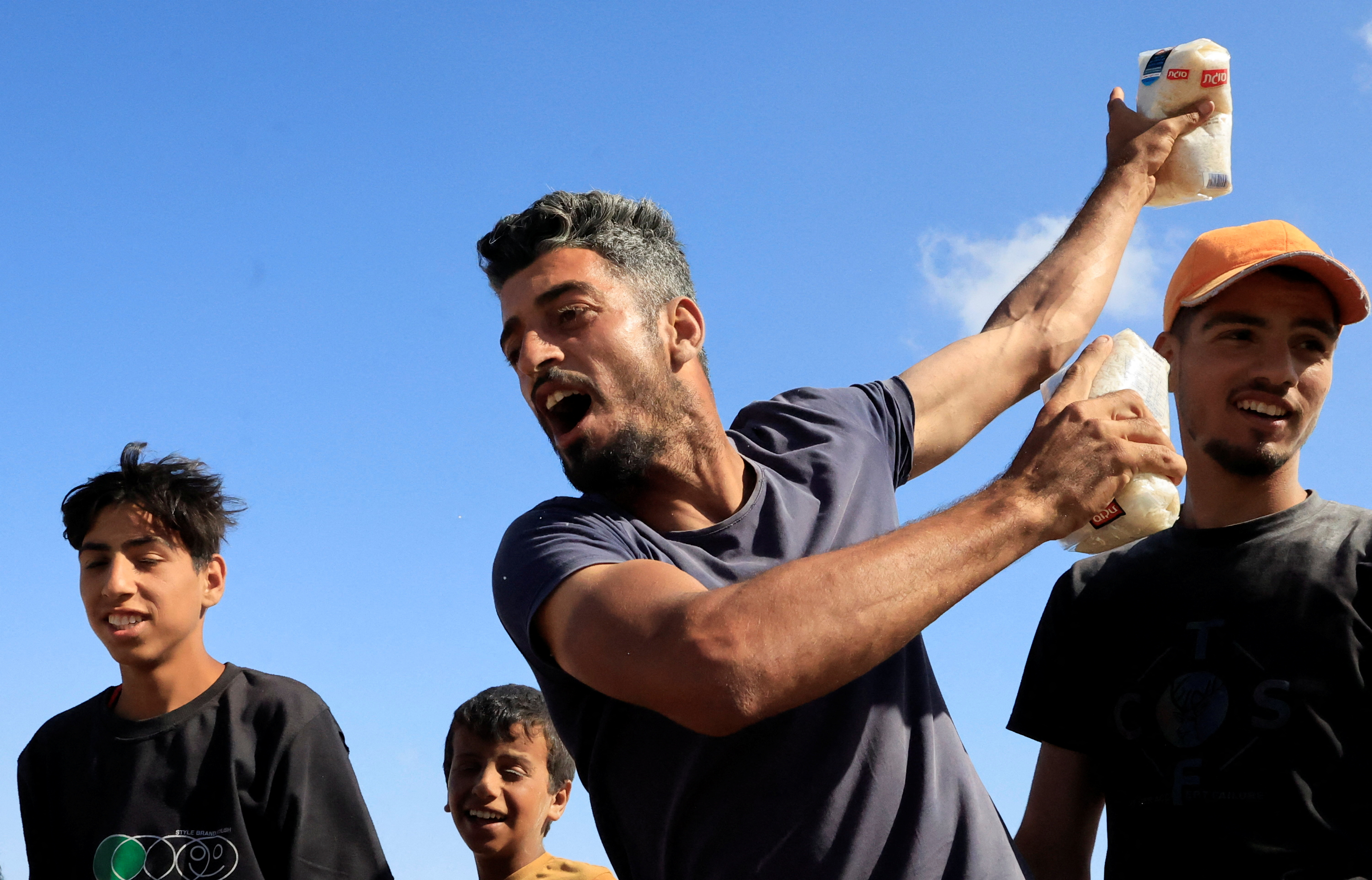 A man with a package of rice in each hand gestures in southern Gaza, making a sweeping motion with his arms.