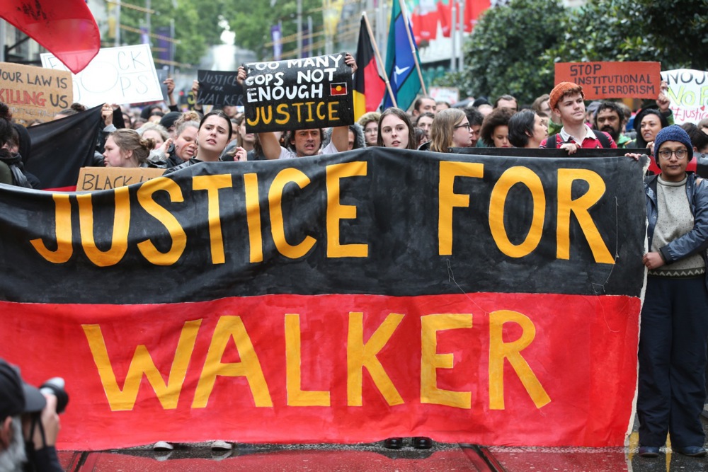 people walk with a red black and yellow banner that says justice for walker