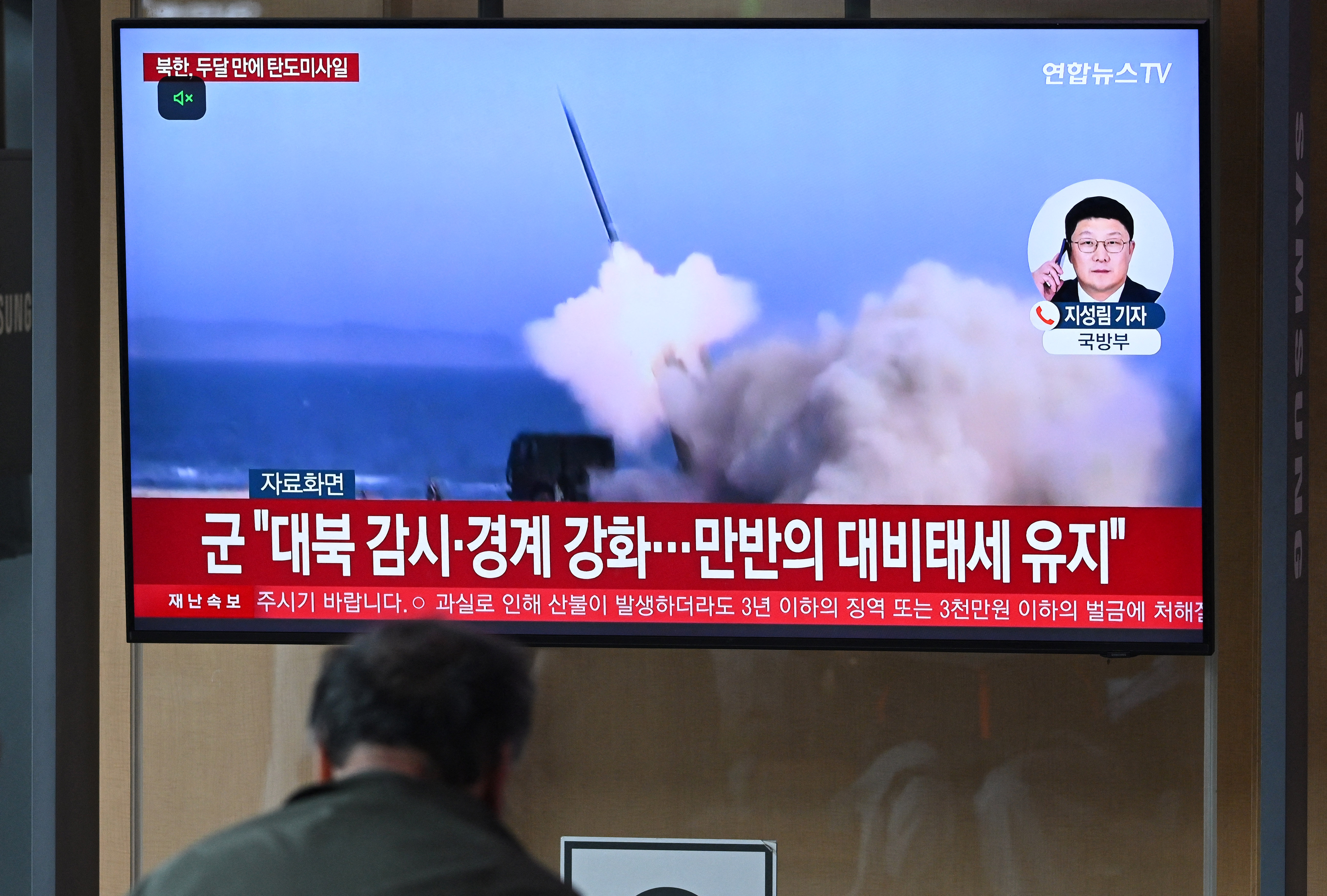 A man watches a television screen showing a news broadcast with file footage of a North Korean missile test.