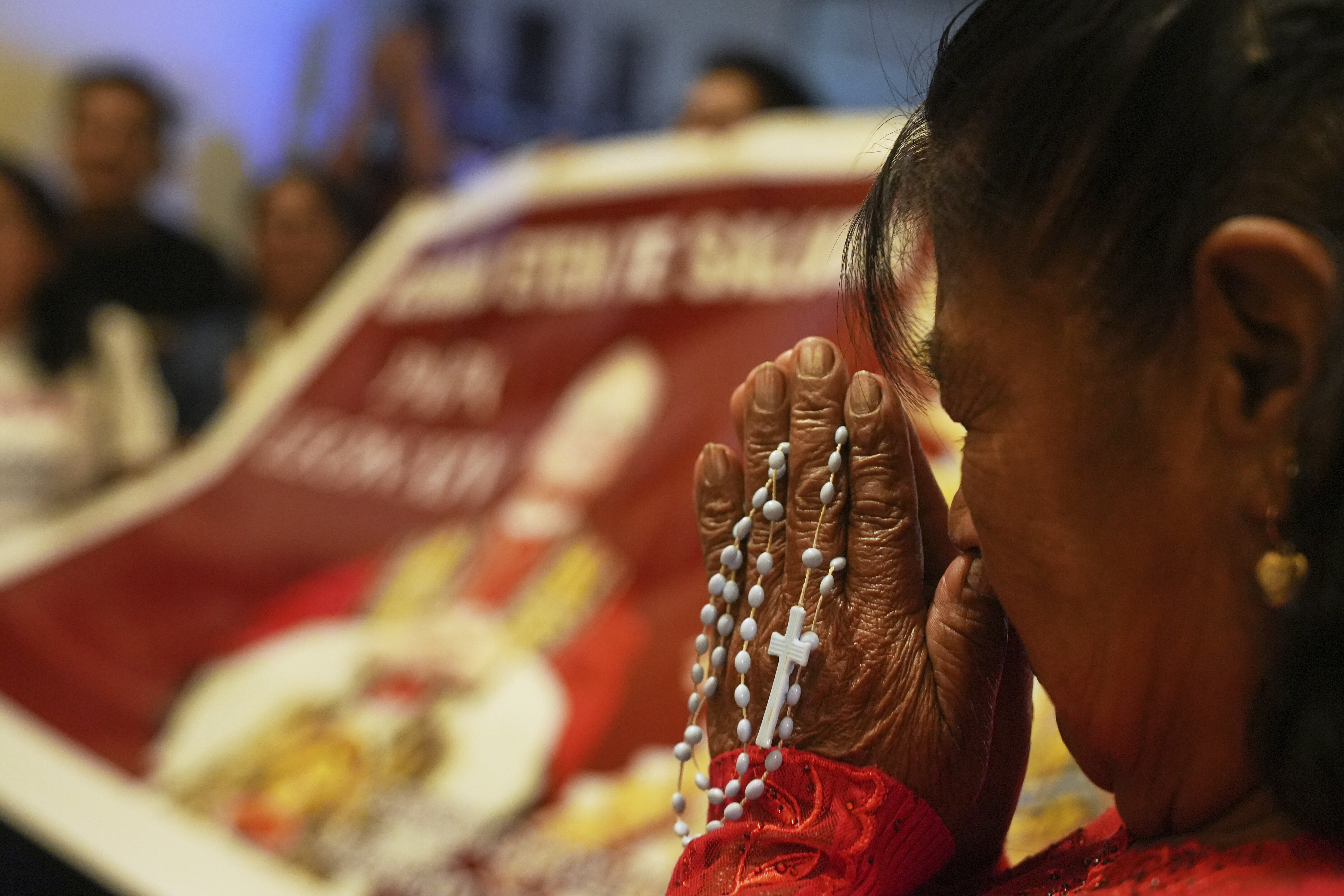 A woman prays with rosary beeds in front of a banner of Pope Leo XIV