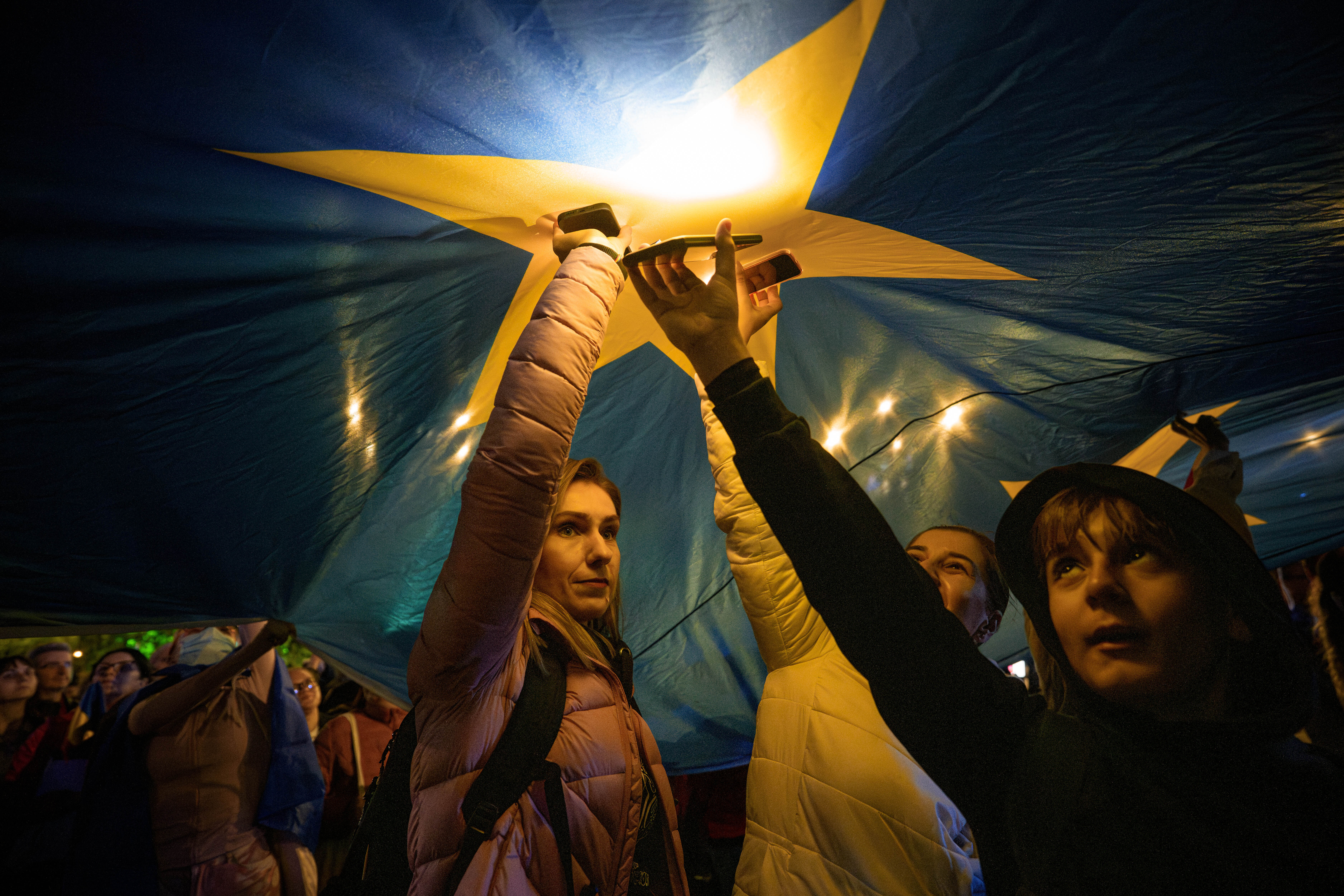 Demonstrators shine the lights of their mobile phones as they stand under a large European Union flag, during a pro-EU rally ahead of the second round of the presidential election redo in Bucharest