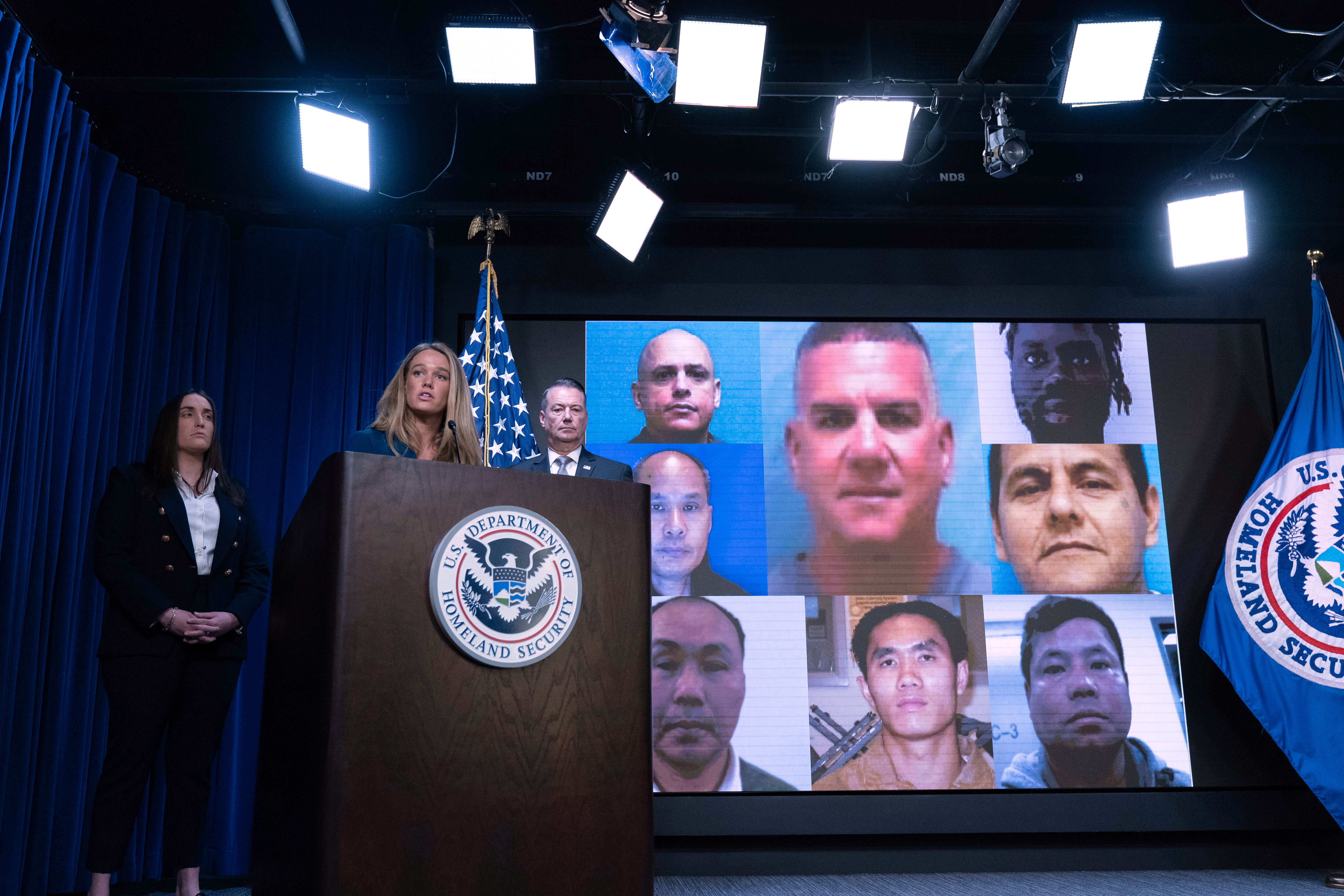 Tricia McLaughlin speaks in front of a series of male portraits, representing migrants the US deported.