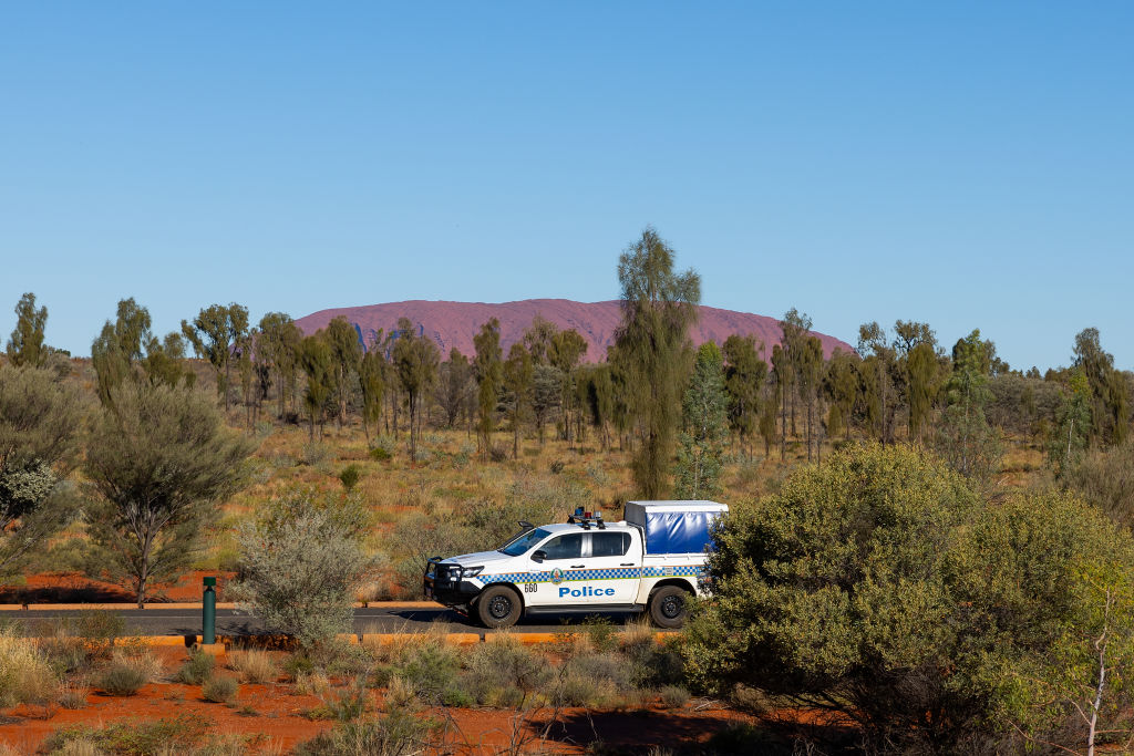 a police car drives near uluru a large red rock in the distance