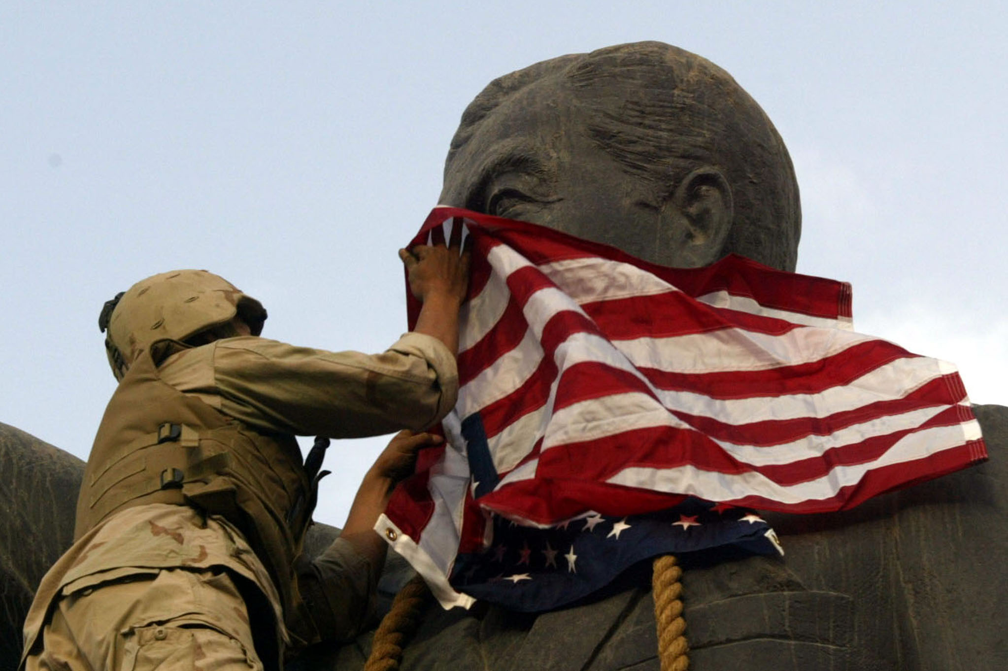 A US Marine covers the face of a statue of Iraqi President Saddam Hussein with a US flag in Baghdad April 9, 2003 [Goran Tomasevic/Reuters]