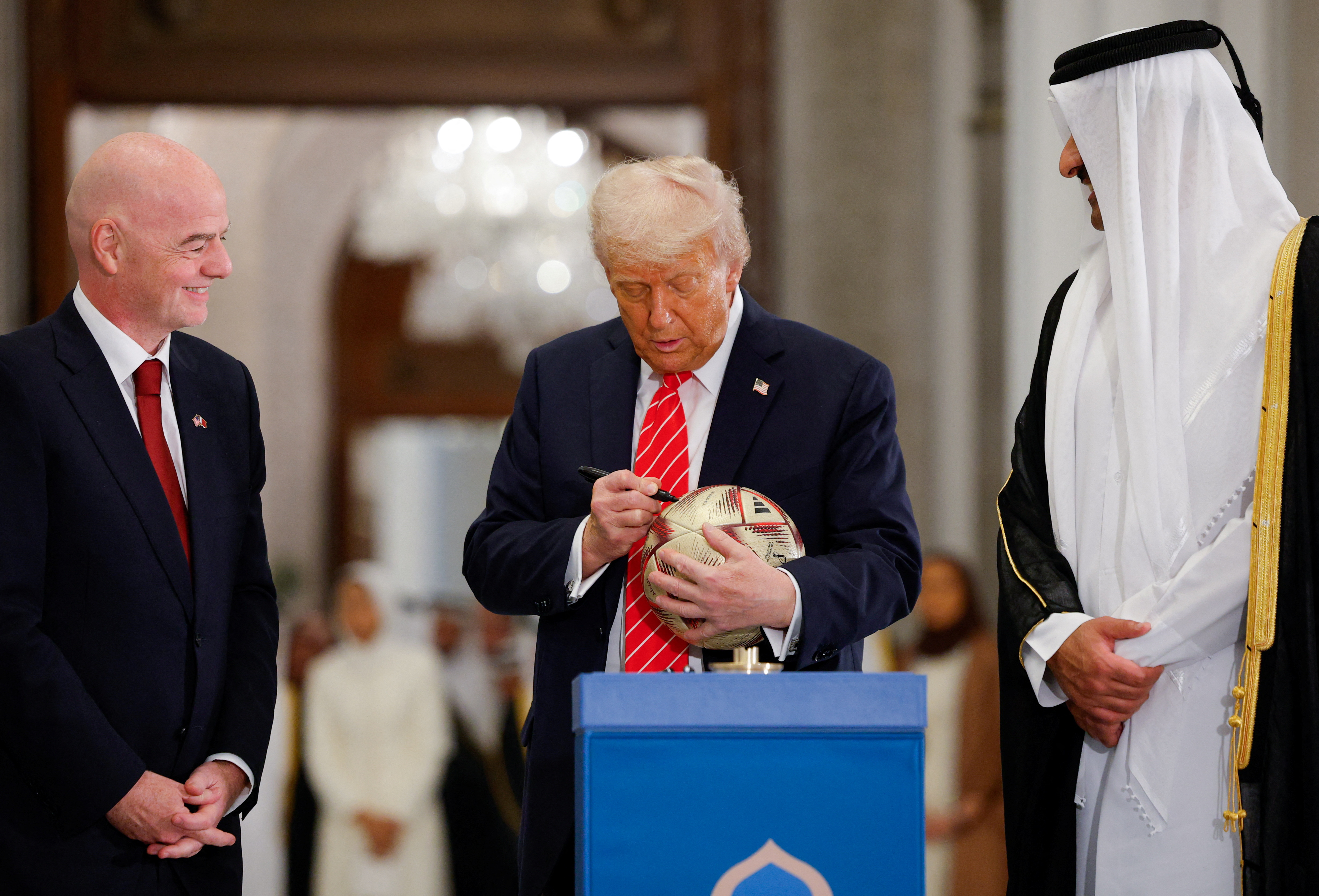 U.S. President Donald Trump writes on a soccer ball as he attends an event with Qatar's Emir Tamim bin Hamad Al Thani and FIFA President Gianni Infantino, at Lusail Palace in Lusail, Qatar, May 14, 2025. 