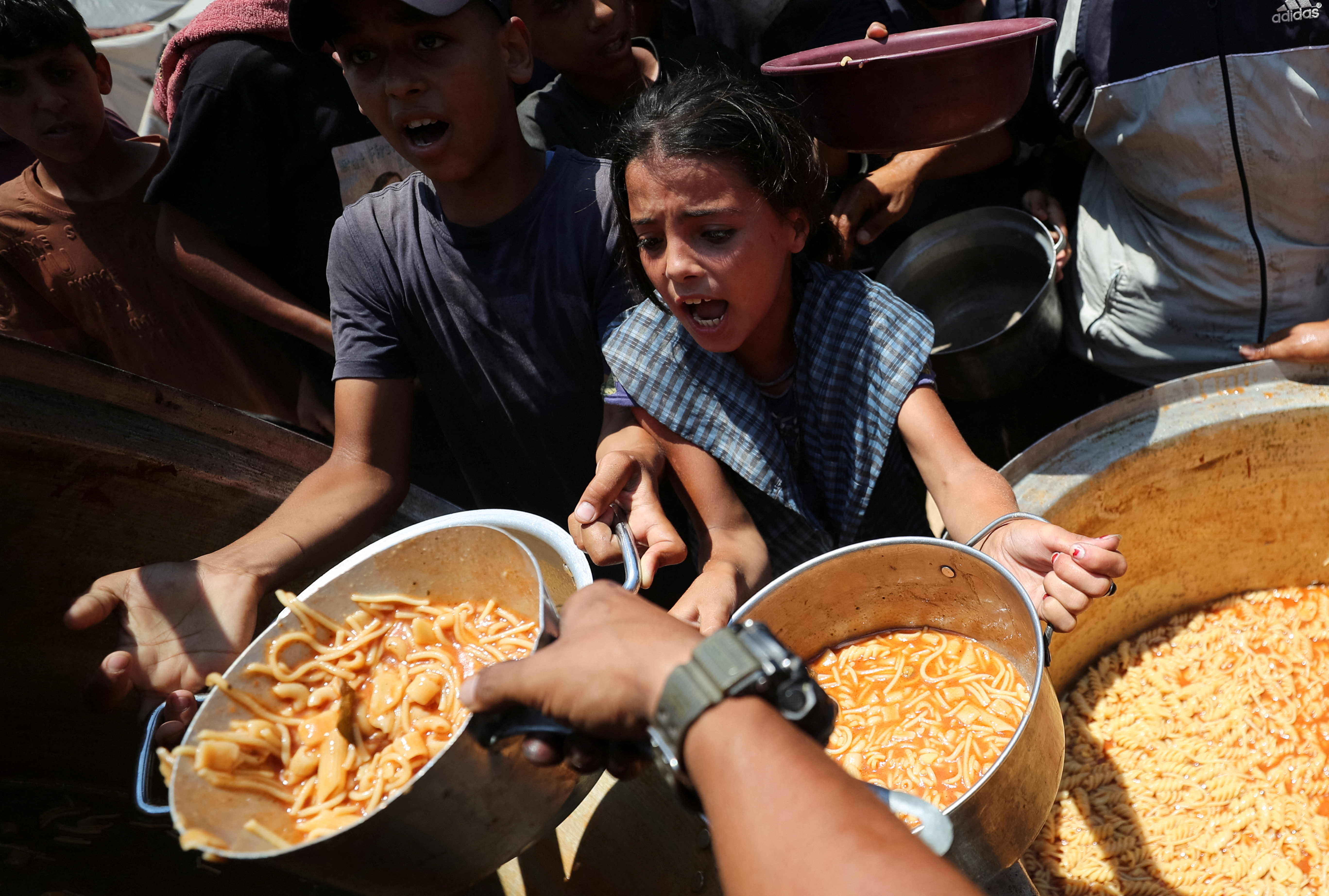 Palestinian children react as they receive food cooked by a charity kitchen