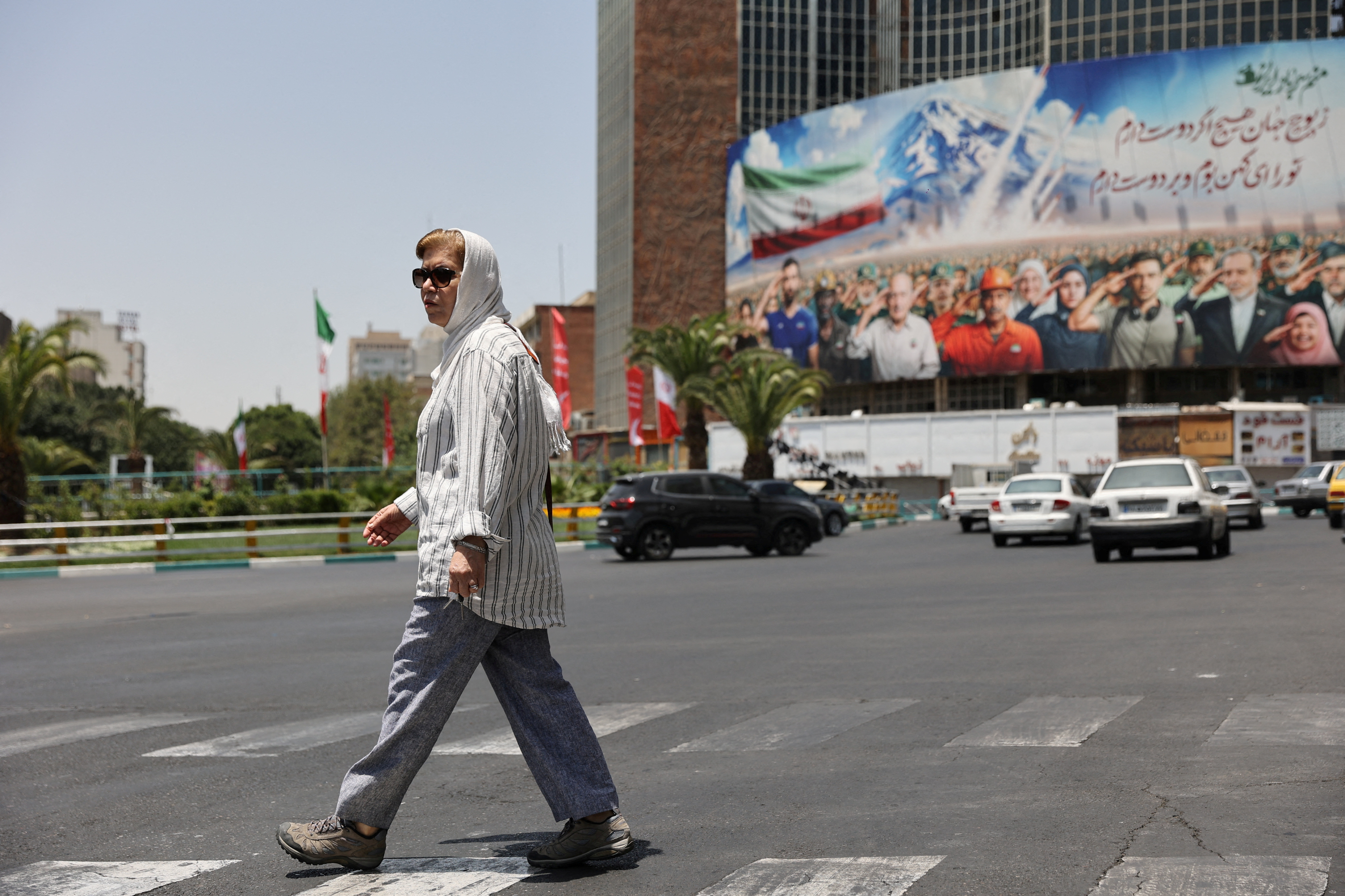A woman walks next to a billboard with a picture of Iranians supporting their country
