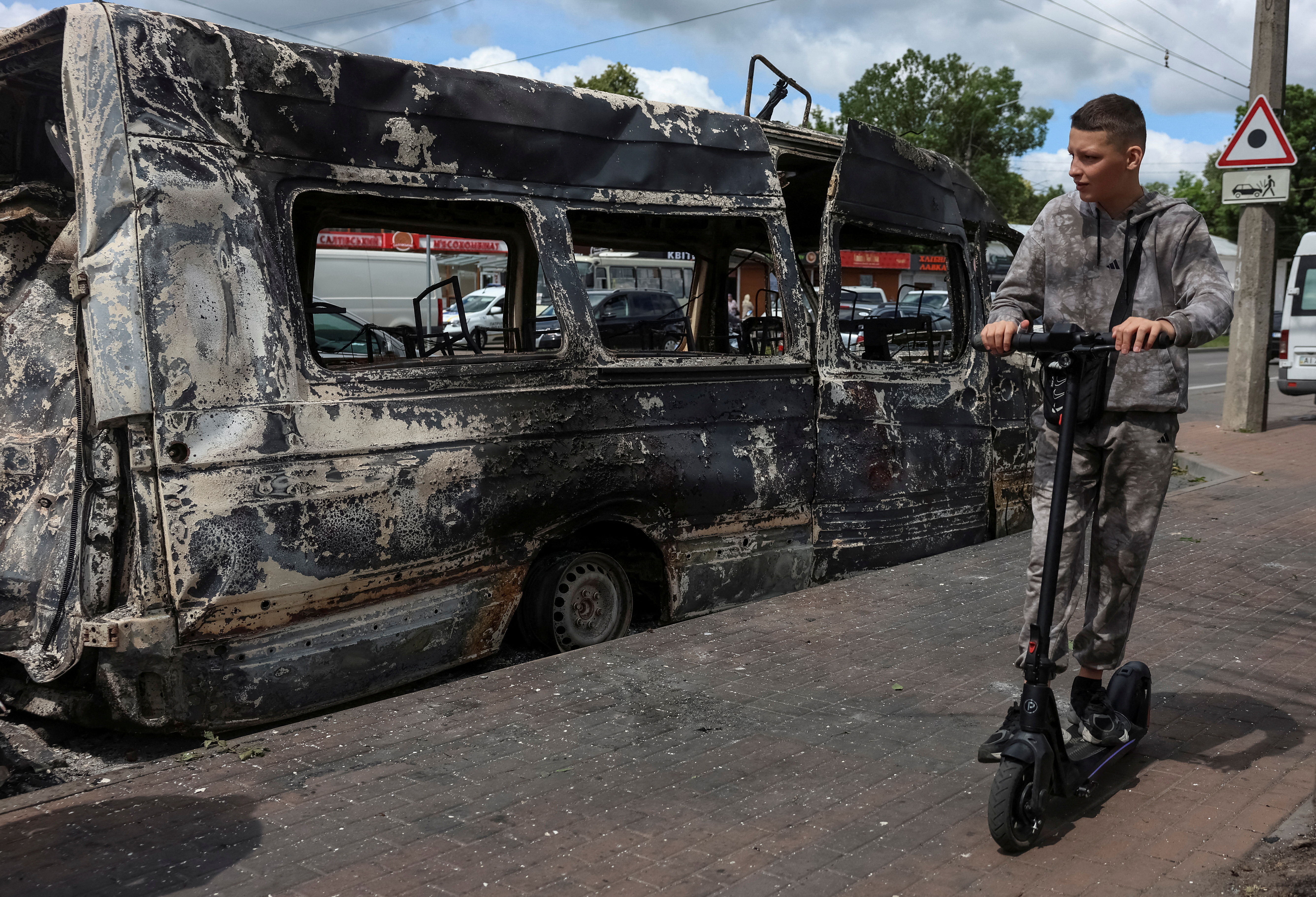 A boy rides a scooter near a vehicle destroyed in the Russian drone and missile strike, amid Russia's attack on Ukraine, in the city of Bila Tserkva in Kyiv region, Ukraine June 23, 2025. REUTERS/Anatolii Stepanov TPX IMAGES OF THE DAY