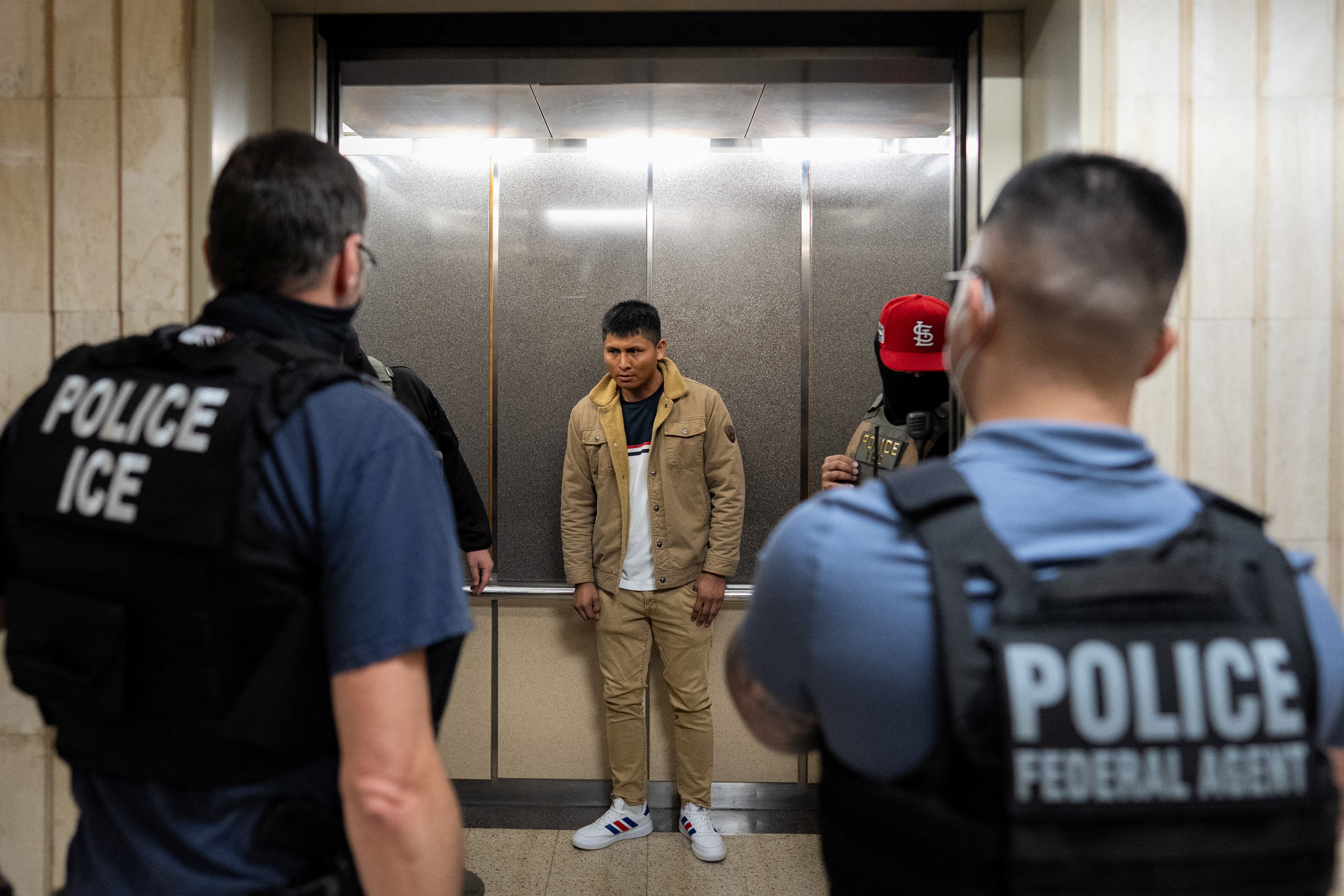A young man stands in between ICE and police officers in an elevator outside of immigration court.