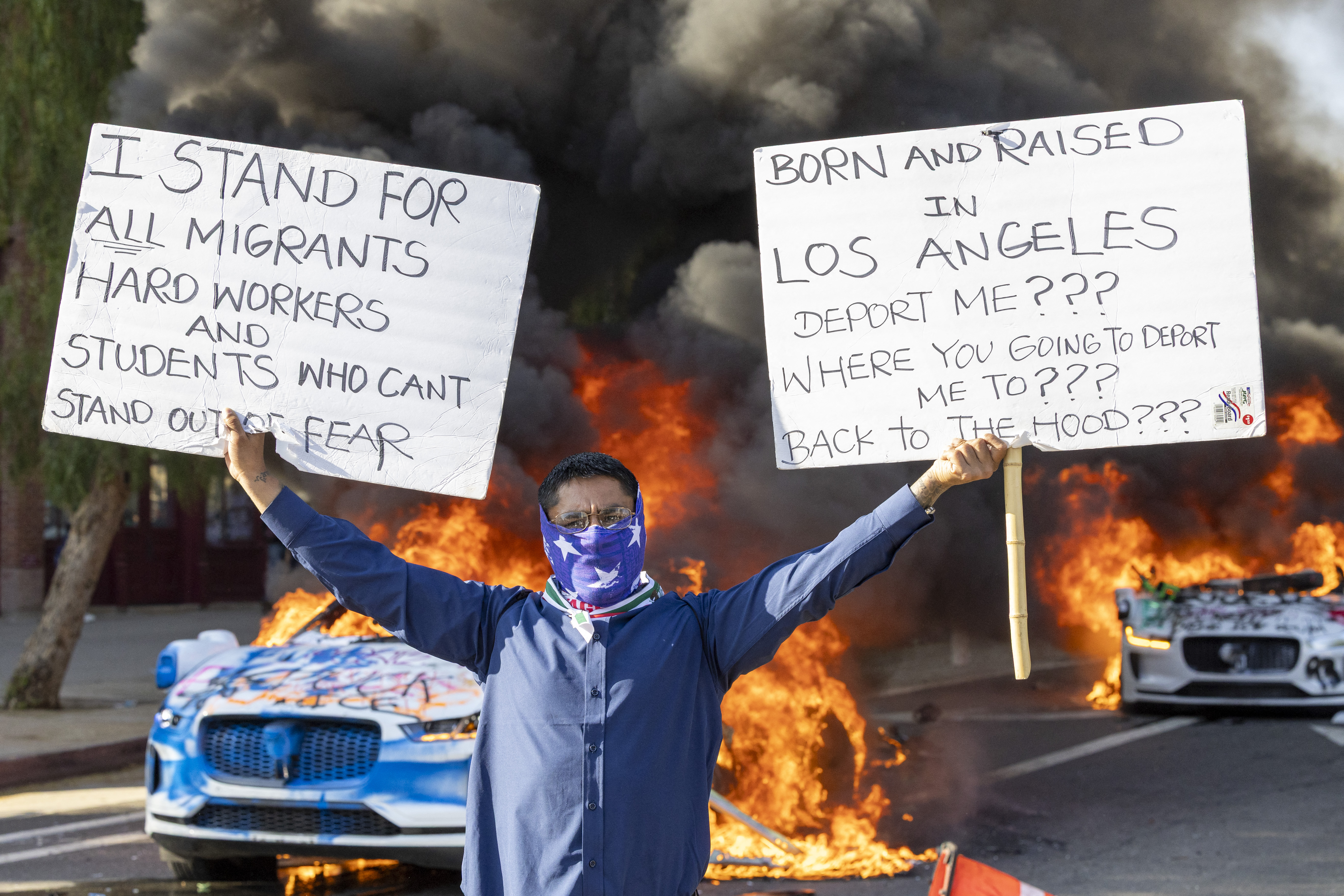 A man holds signs as a Waymo vehicles burn