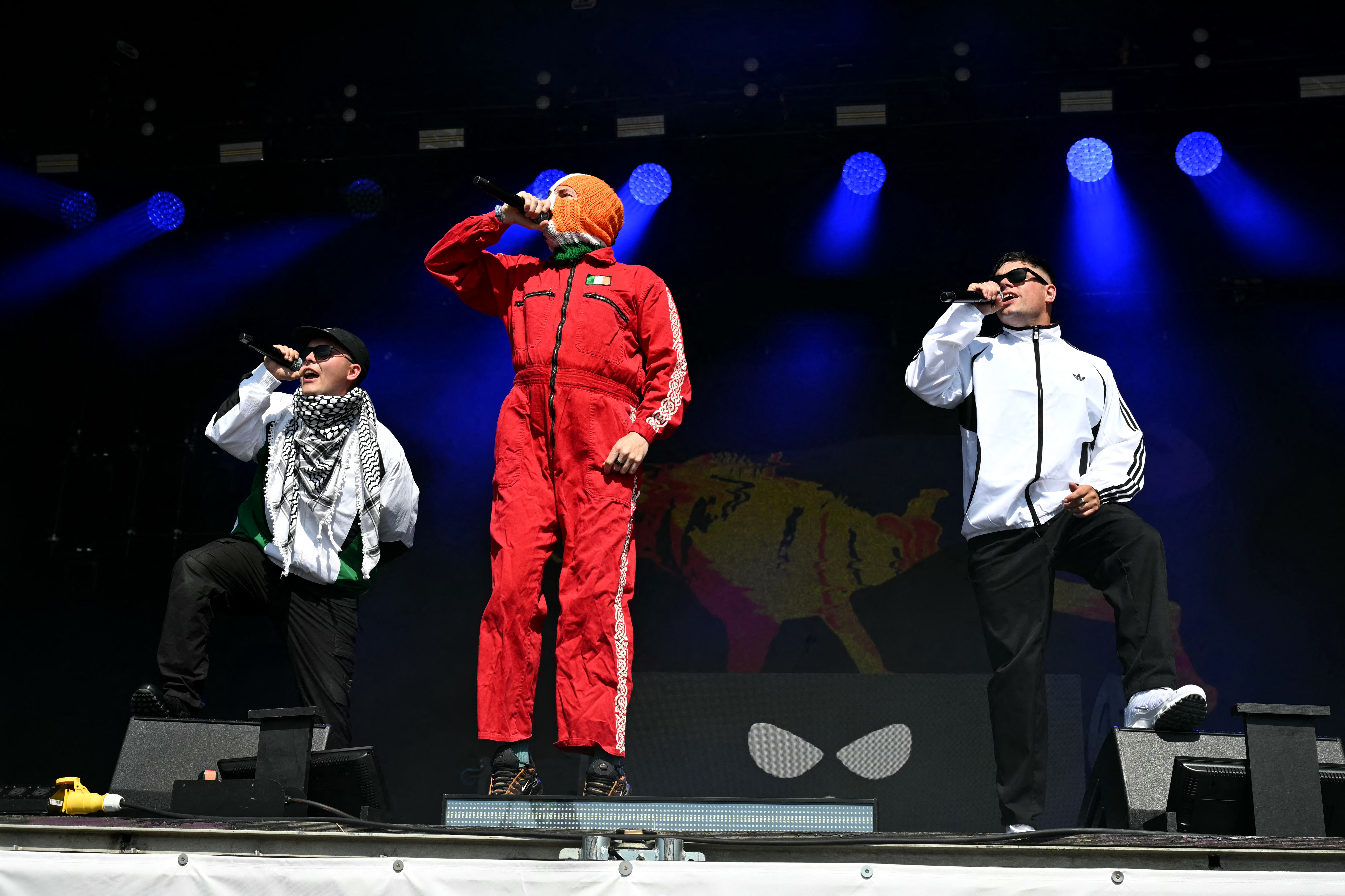 a mane in a red tracksuit and Irish flag balaclava sings next to another man wearing a keffiyeh