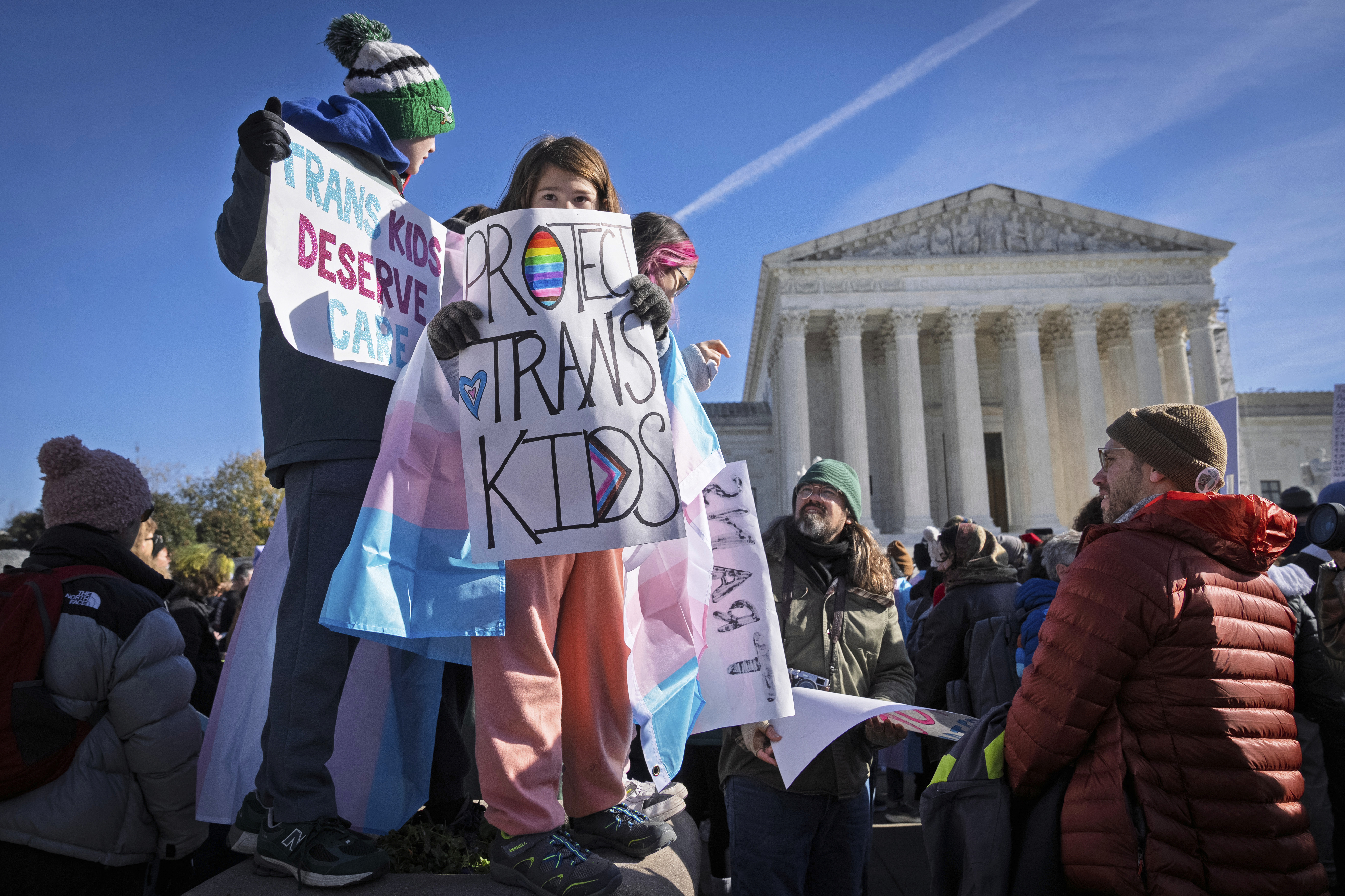 Youth protesters stand outside the Supreme Court with signs calling to 'protect trans kids'.