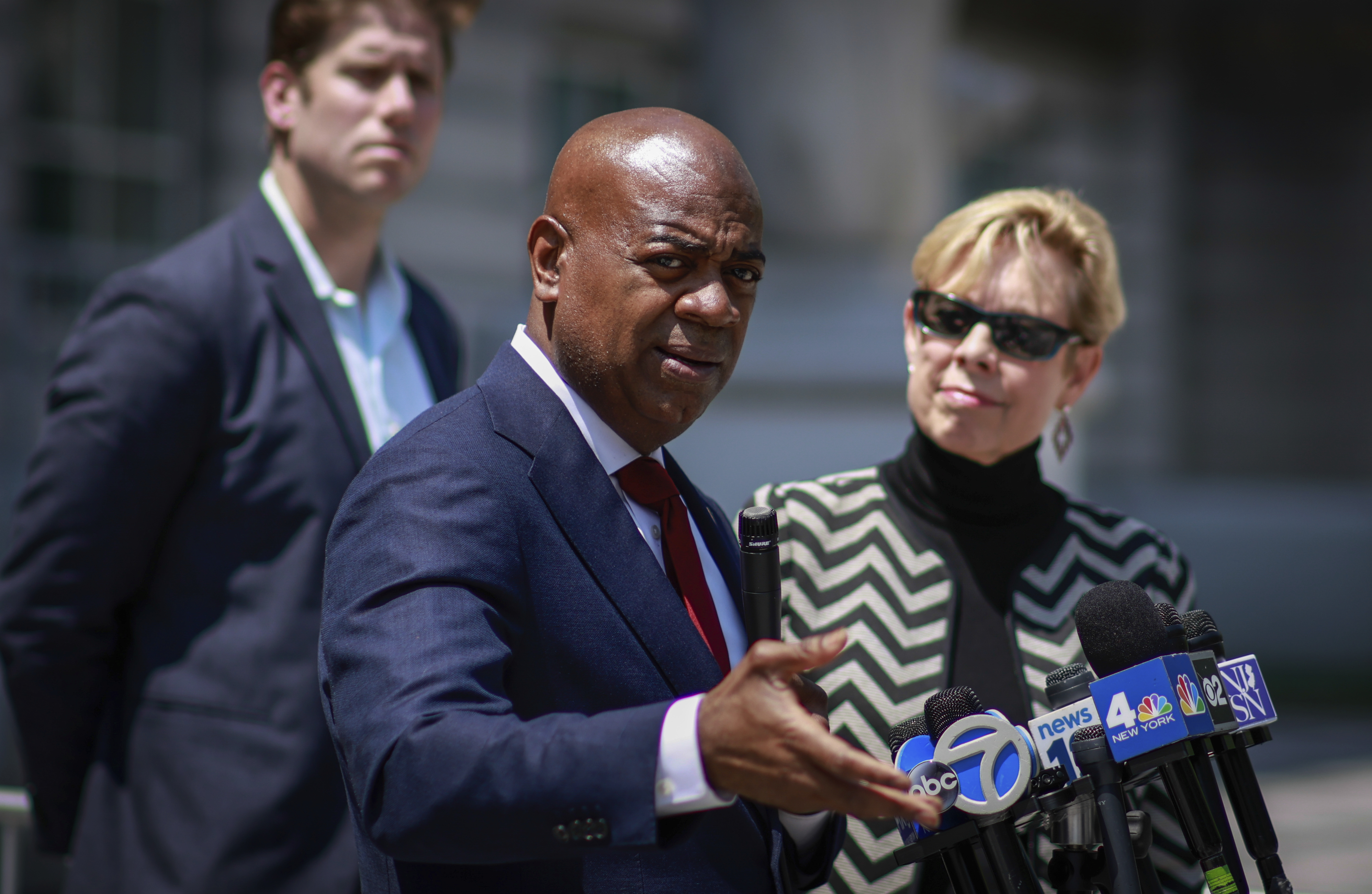 Newark Mayor Ras Baraka gestures as he speaks into TV news microphones during an outdoor press conference.