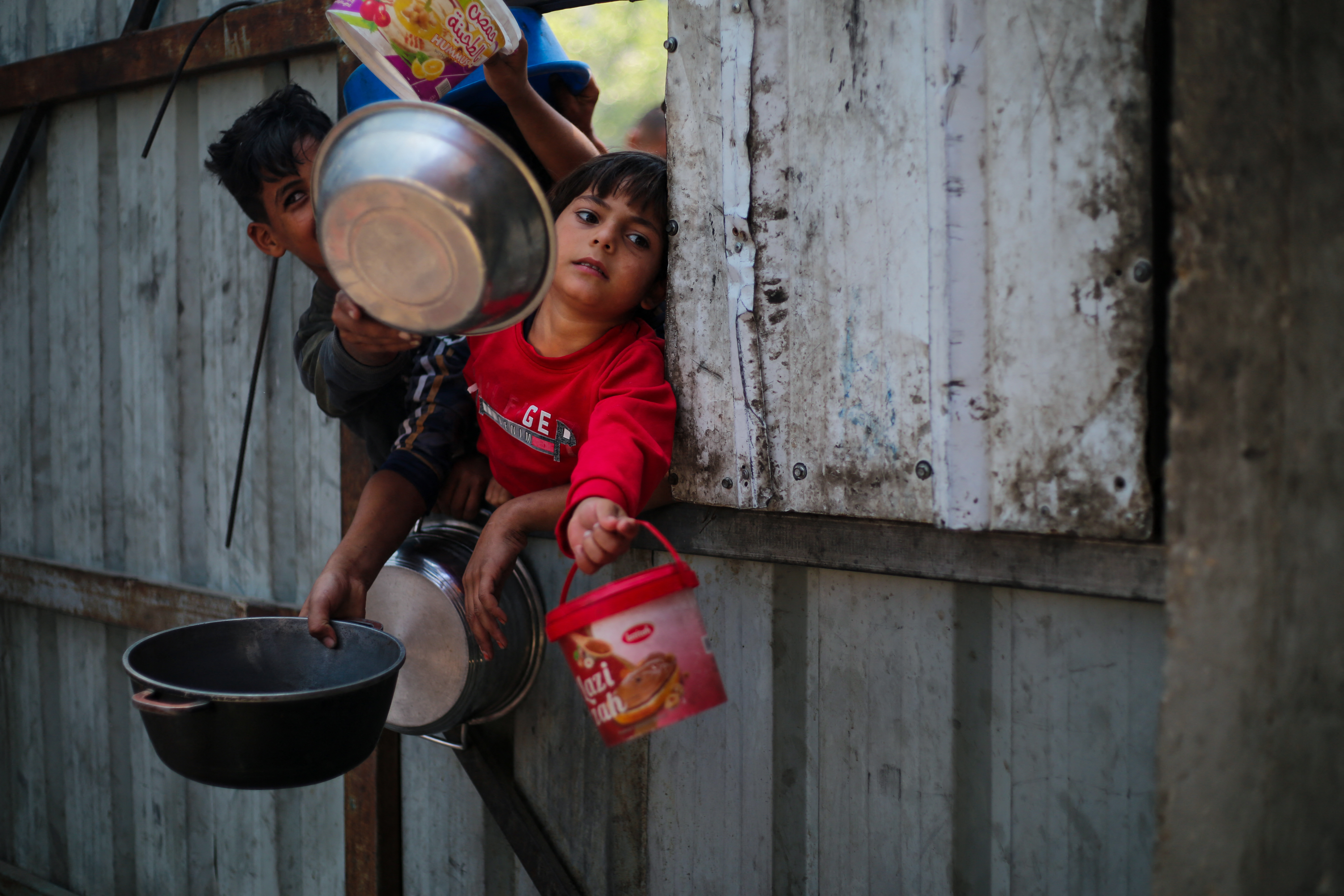 Palestinian children reach out with their pots as they wait for food at a distribution point in Nuseirat, central Gaza Strip, June 2, 2025.