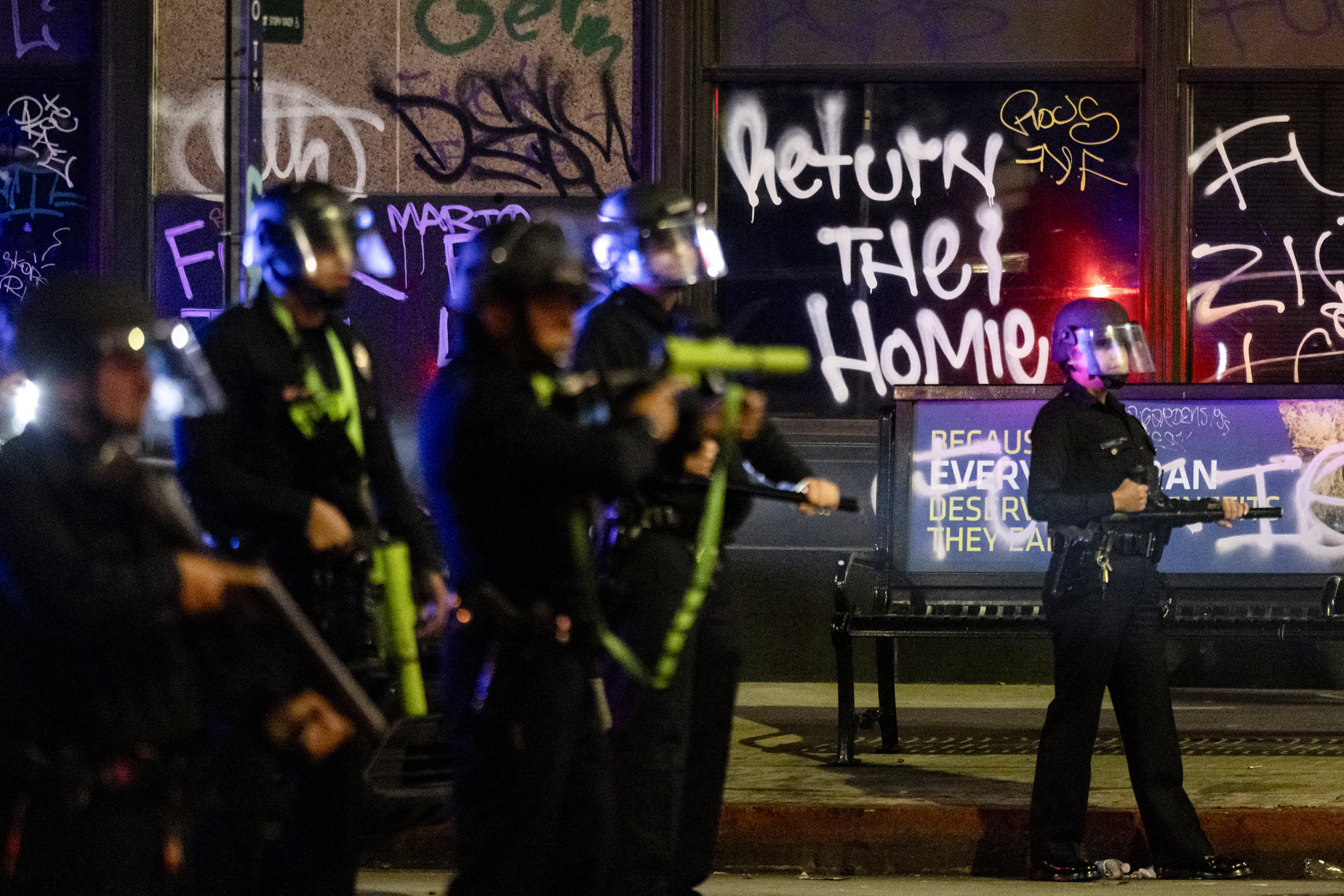 A graffiti reads “Return the Homies” behind Los Angeles police officers deployed next to City Hall as clashes with protesters continue into the night during a protest following federal immigration operations, in Los Angeles, California on June 8, 2025.