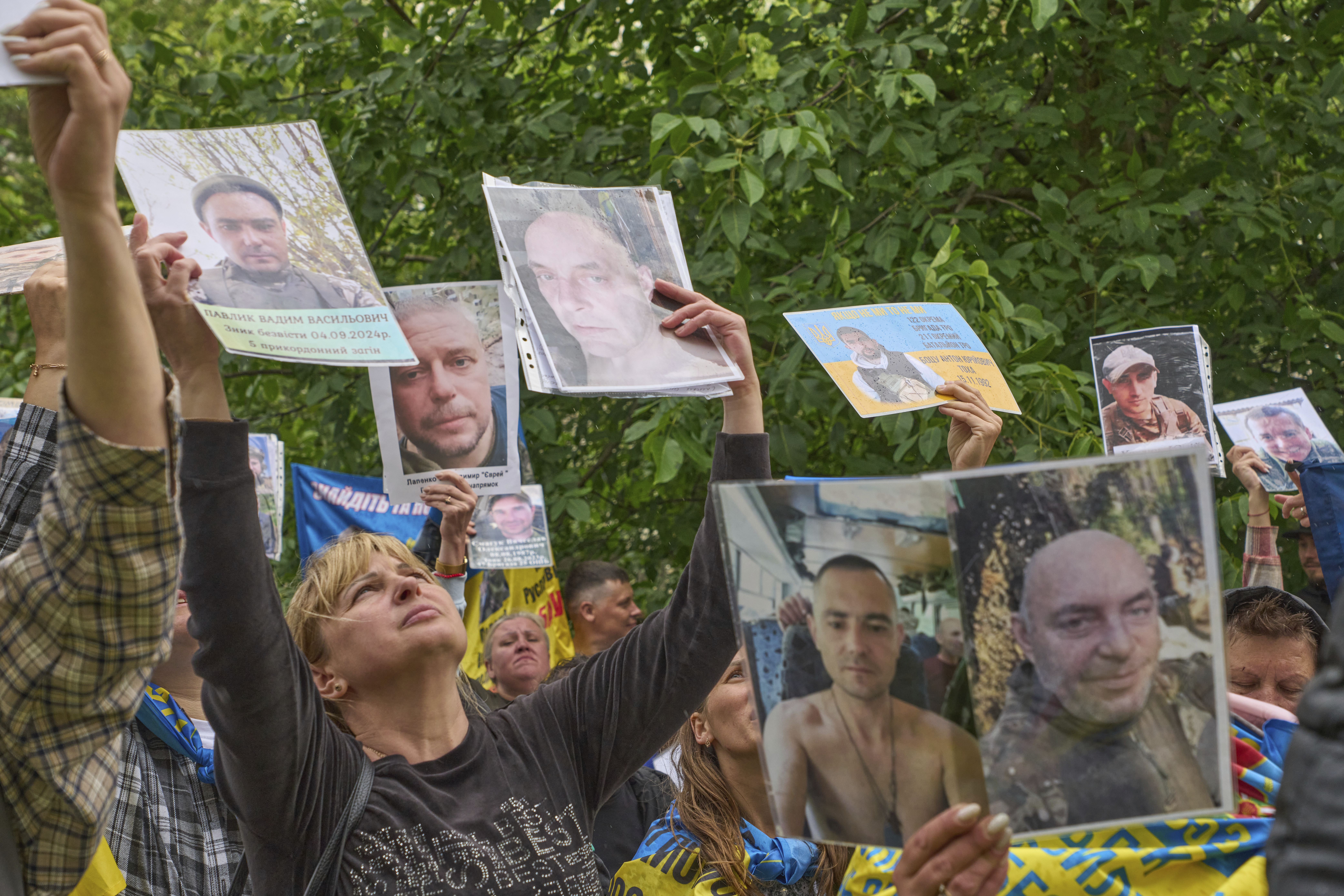 People hold up photos of their missing relatives to Ukrainian soldiers in Chernyhiv region, Ukraine, returning after a POW exchange between Russia and Ukraine, Thursday, June 12, 2025. (AP Photo/Efrem Lukatsky)
