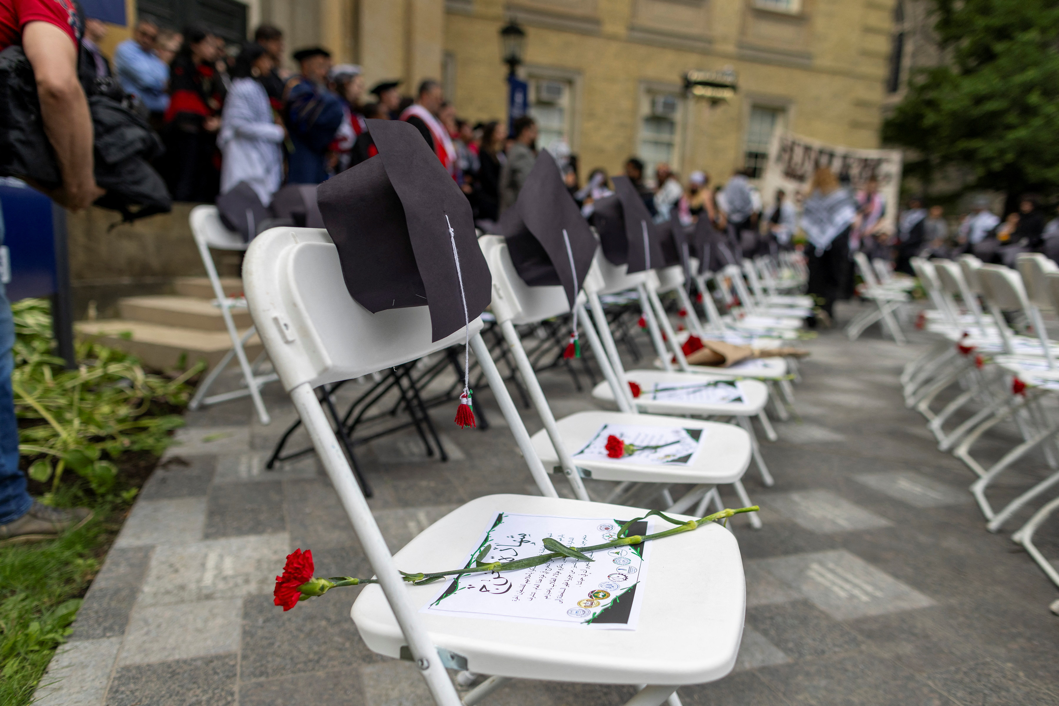 Flowers, graduation caps and certificates in Arabic are placed on white chairs on a university lawn.