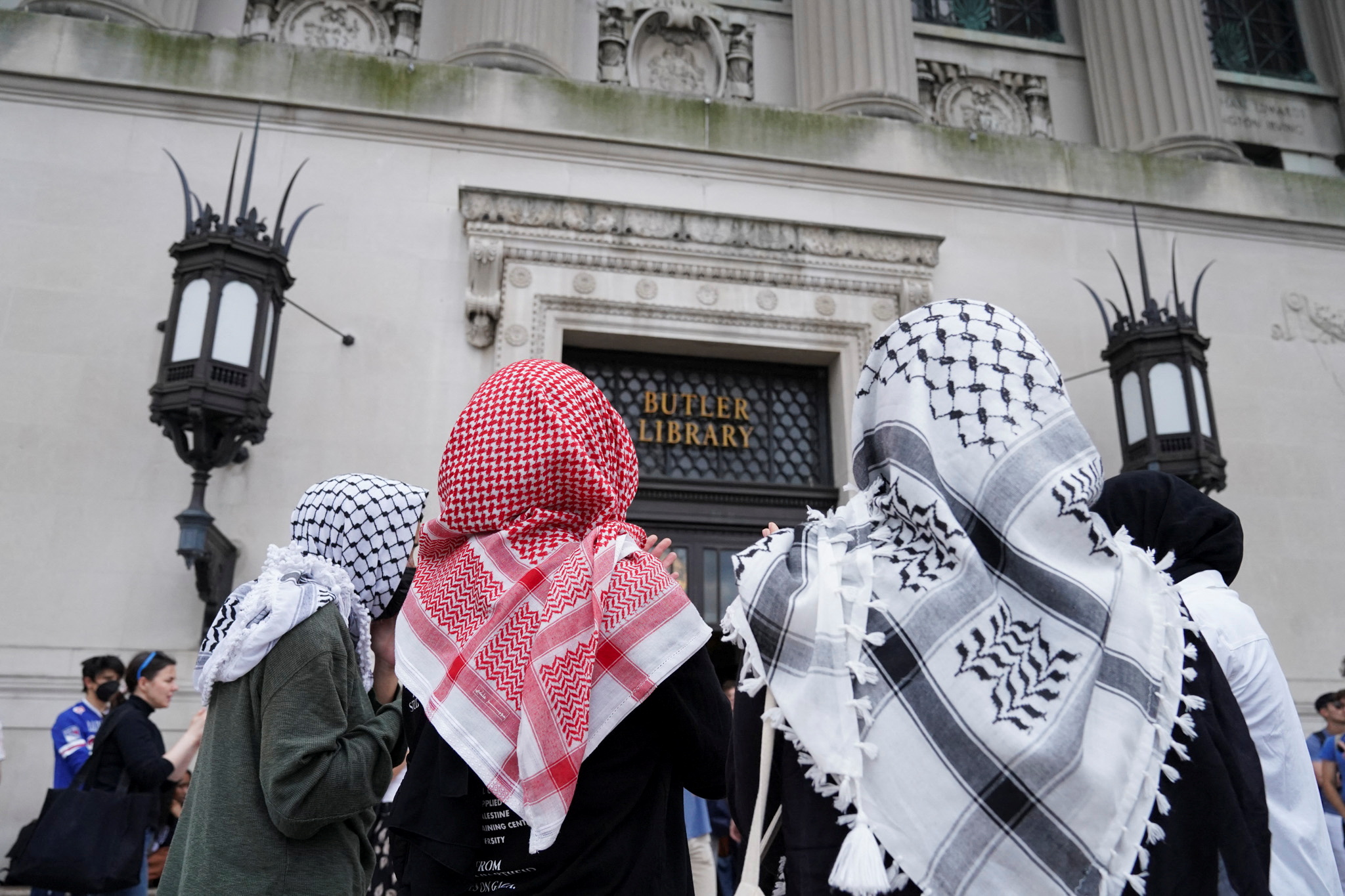 three people wearing keffiyeh scarfs on their heads stand in front of an old building named the butler library